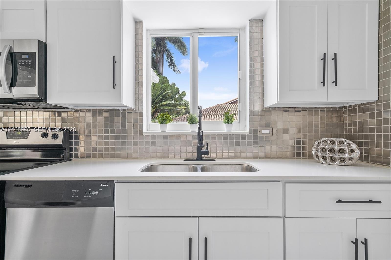 Kitchen featuring white shaker-style cabinetry, matte black hardware, stainless steel appliances, quartz countertops, and a metallic mosaic tile backs