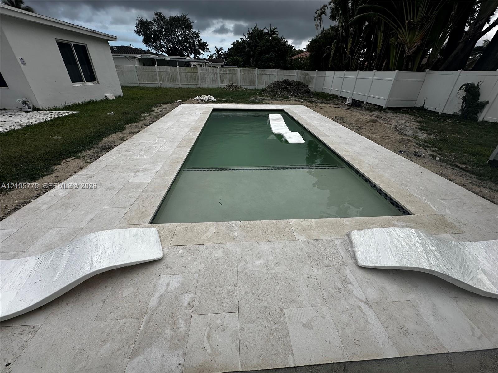 Rectangular in-ground pool with stone paver decking and perimeter vinyl fencing