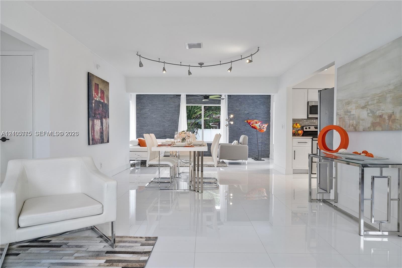 Open-concept interior featuring polished tile flooring, recessed track lighting, and a prominent dark stone-textured accent wall