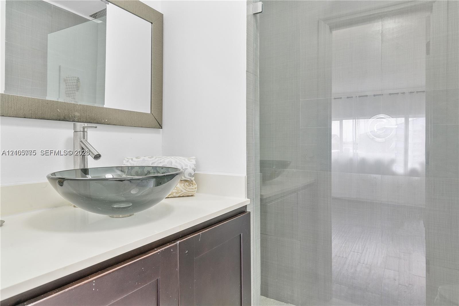 Bathroom vanity featuring a dark-finish wood cabinet, solid-surface countertop, glass vessel sink, and a framed wall mirror, accompanied by a glass-en