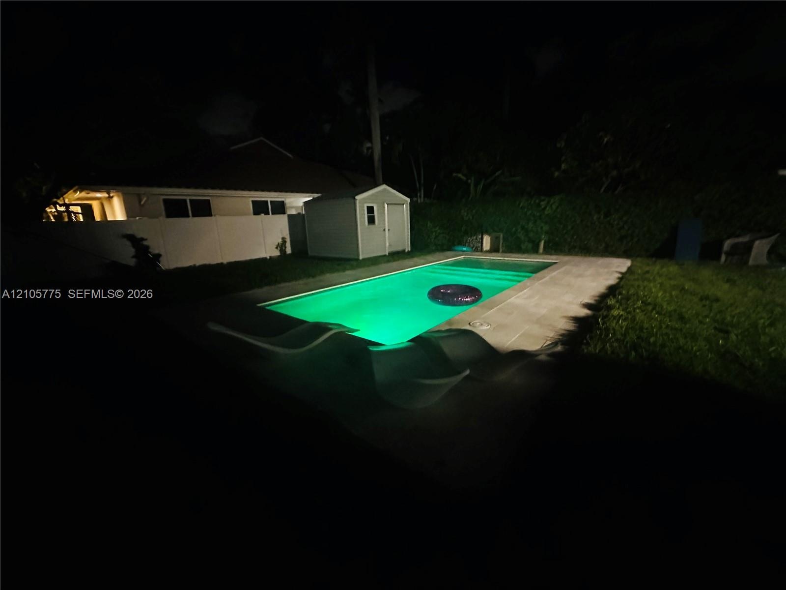 In-ground swimming pool with surrounding concrete patio, enclosed by vinyl privacy fencing and featuring a detached storage structure