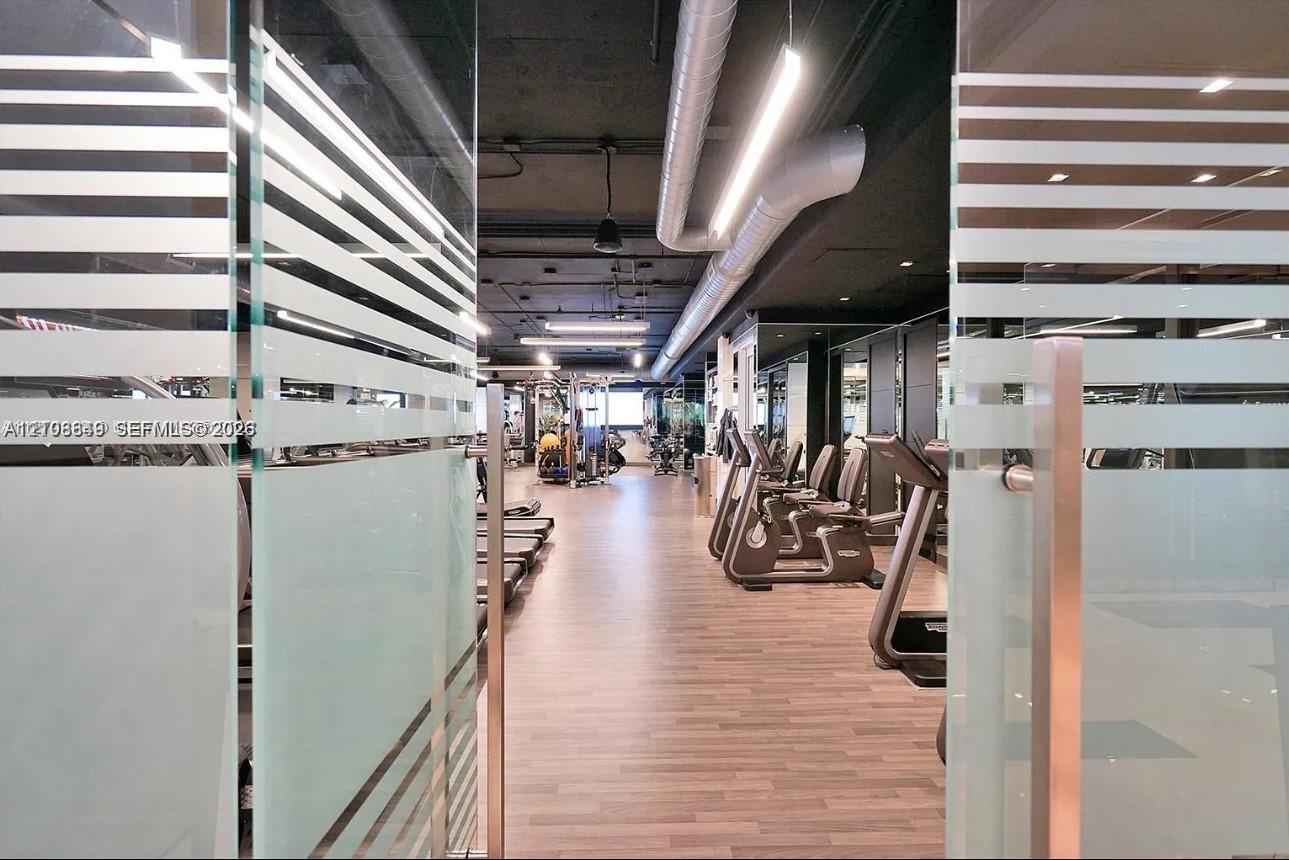 Glass doors with frosted horizontal detailing, wood-finish flooring, exposed industrial-style ceiling with ductwork, and linear overhead lighting
