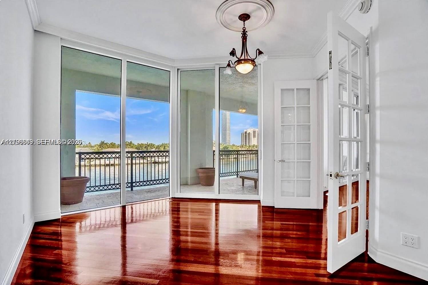 Room featuring polished wood-finish flooring, floor-to-ceiling glass paneling, a decorative ceiling medallion with an attached chandelier, and French-