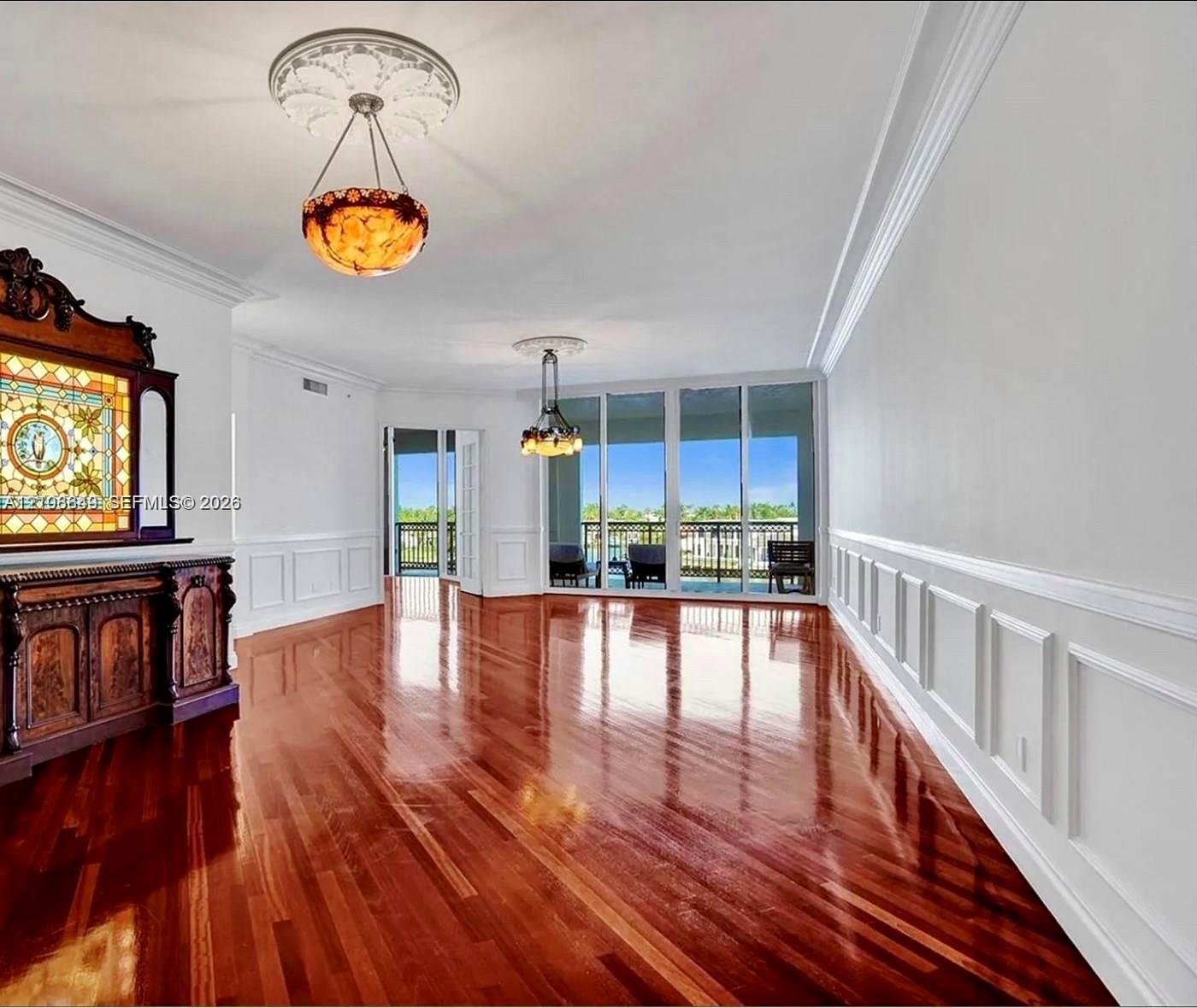 Polished wood-finish flooring, extensive wainscoting, ornate ceiling medallions, dual hanging light fixtures, and floor-to-ceiling glass sliding doors