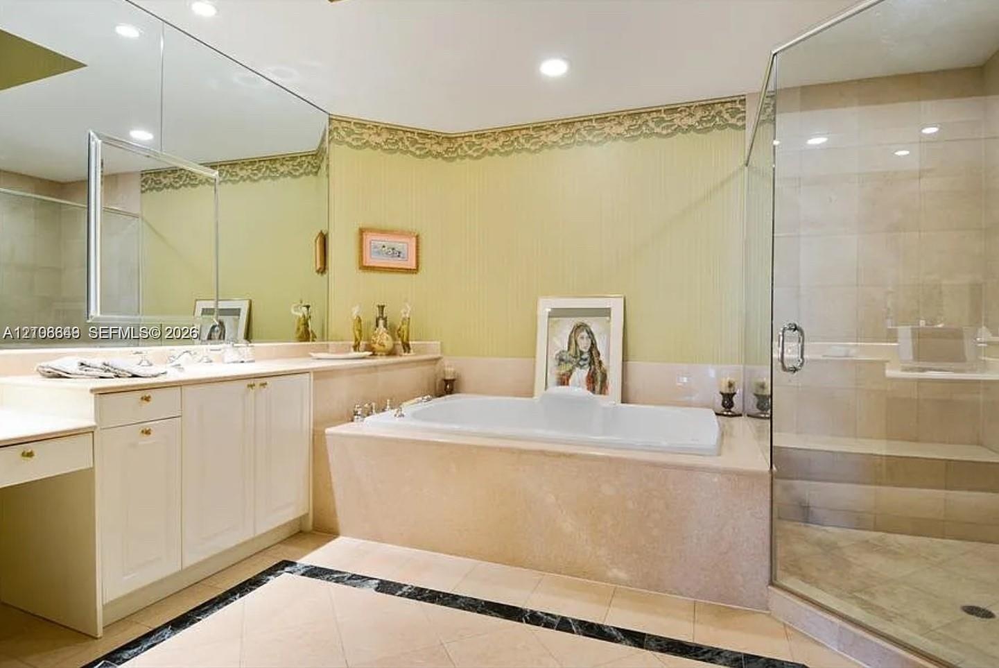 Bathroom featuring a built-in soaking tub, a frameless glass-enclosed shower with tile surround, white cabinetry, a large wall-mounted mirror, and til