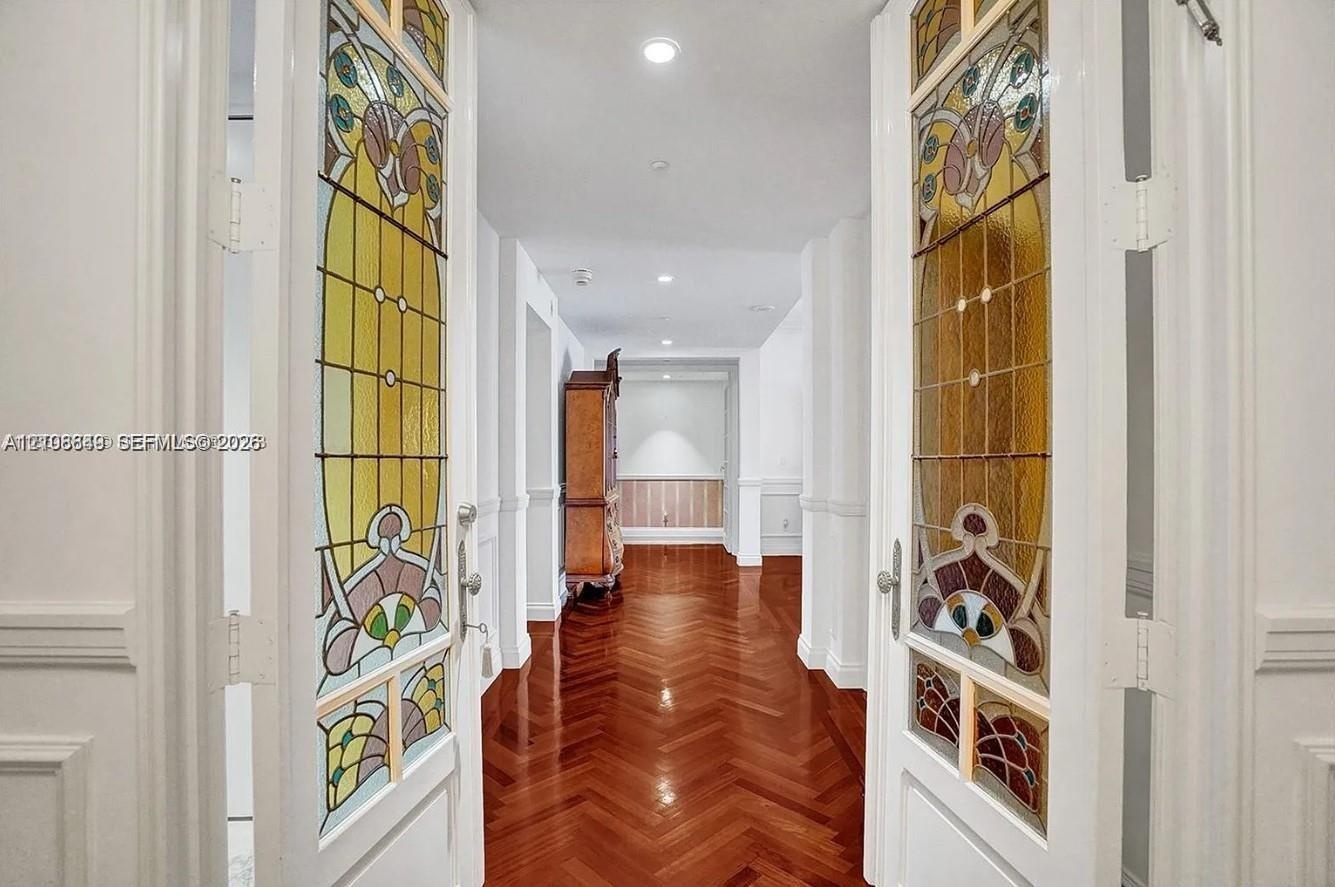 Double doors featuring decorative stained-glass panels, wood-finish flooring laid in a herringbone pattern, wainscoting, and recessed ceiling lighting
