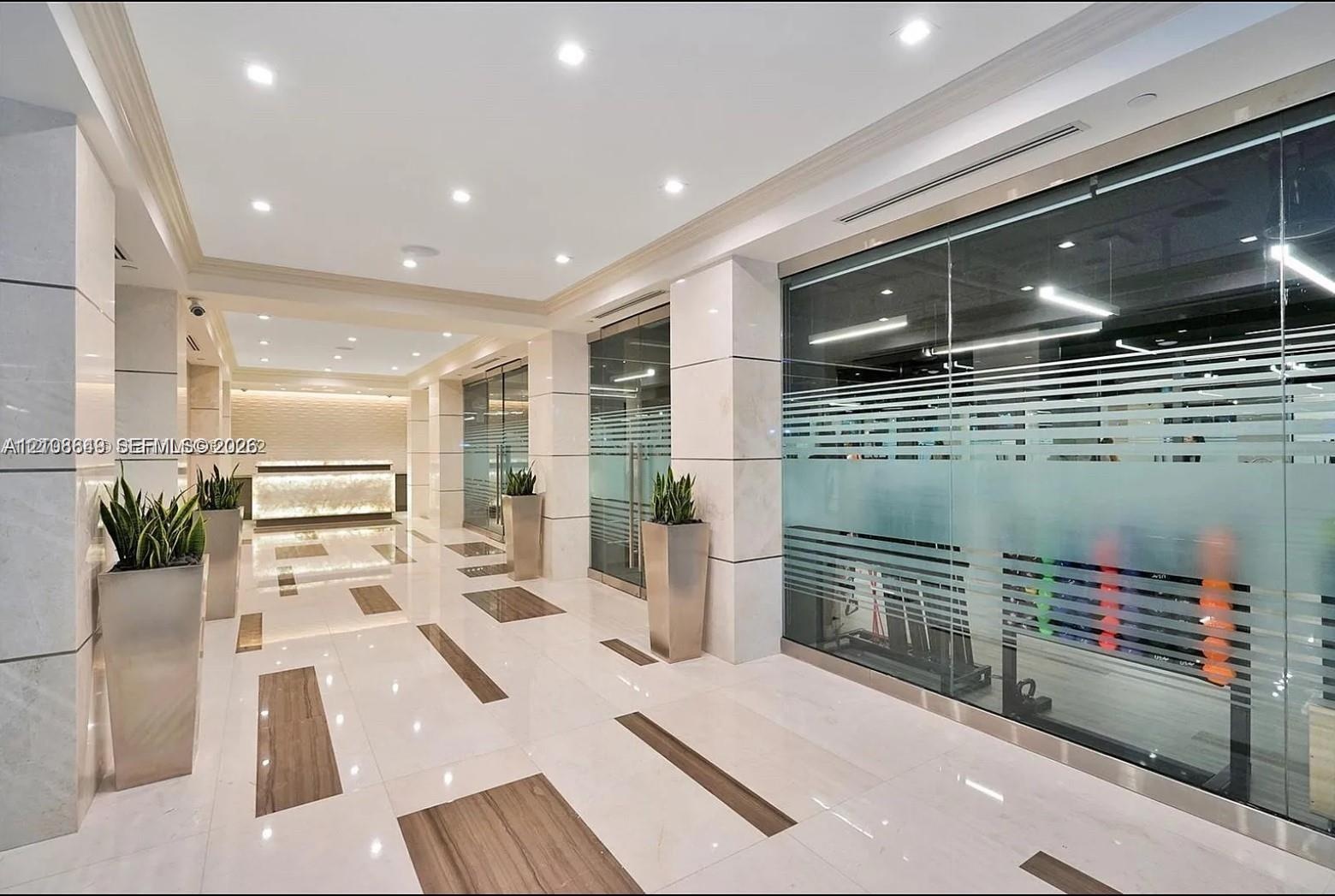 Polished stone flooring with inlaid wood-finish accents, large-format stone pillar cladding, glass-partitioned wall panels, recessed lighting, and a b