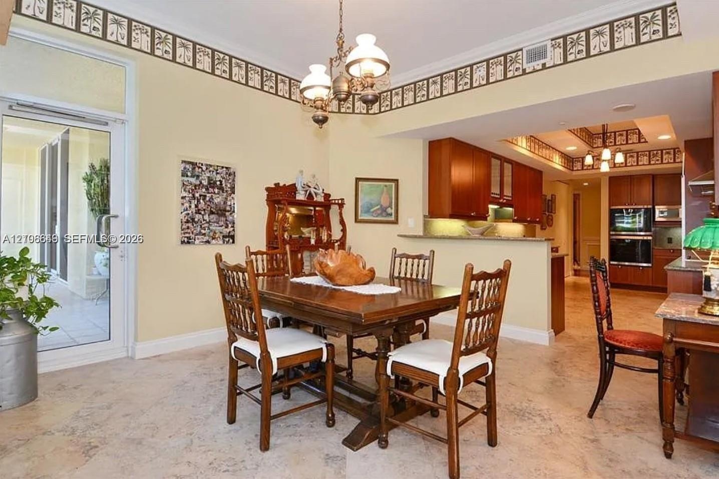 Open-concept dining area featuring stone tile flooring, stained wood cabinetry, recessed lighting, a decorative chandelier, and a full-glass exterior 