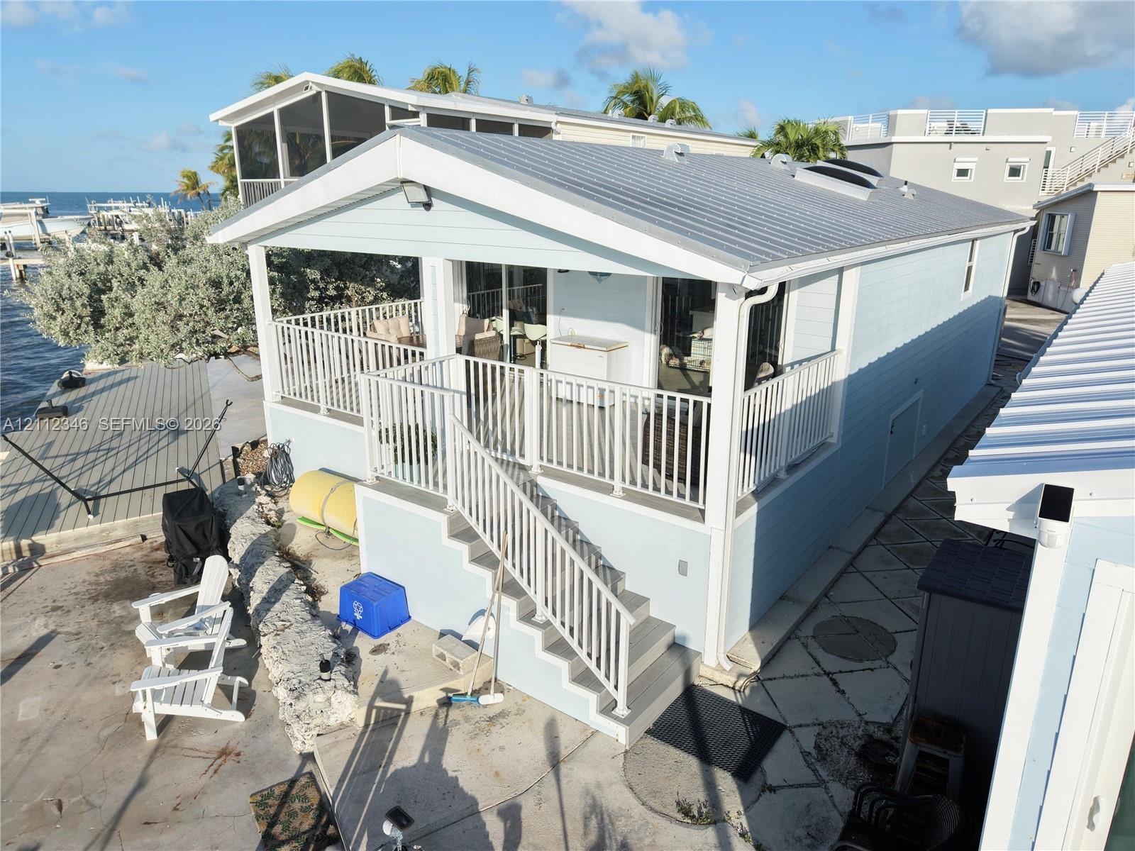 Waterfront property featuring a metal roof, elevated covered deck with white railing, exterior staircase, and siding