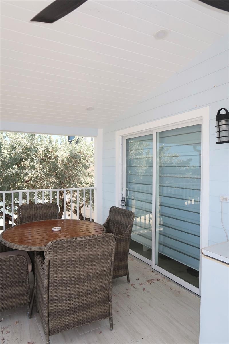 Covered patio featuring beadboard ceiling, horizontal lap siding, white railing, sliding glass doors, and a mounted exterior wall lantern
