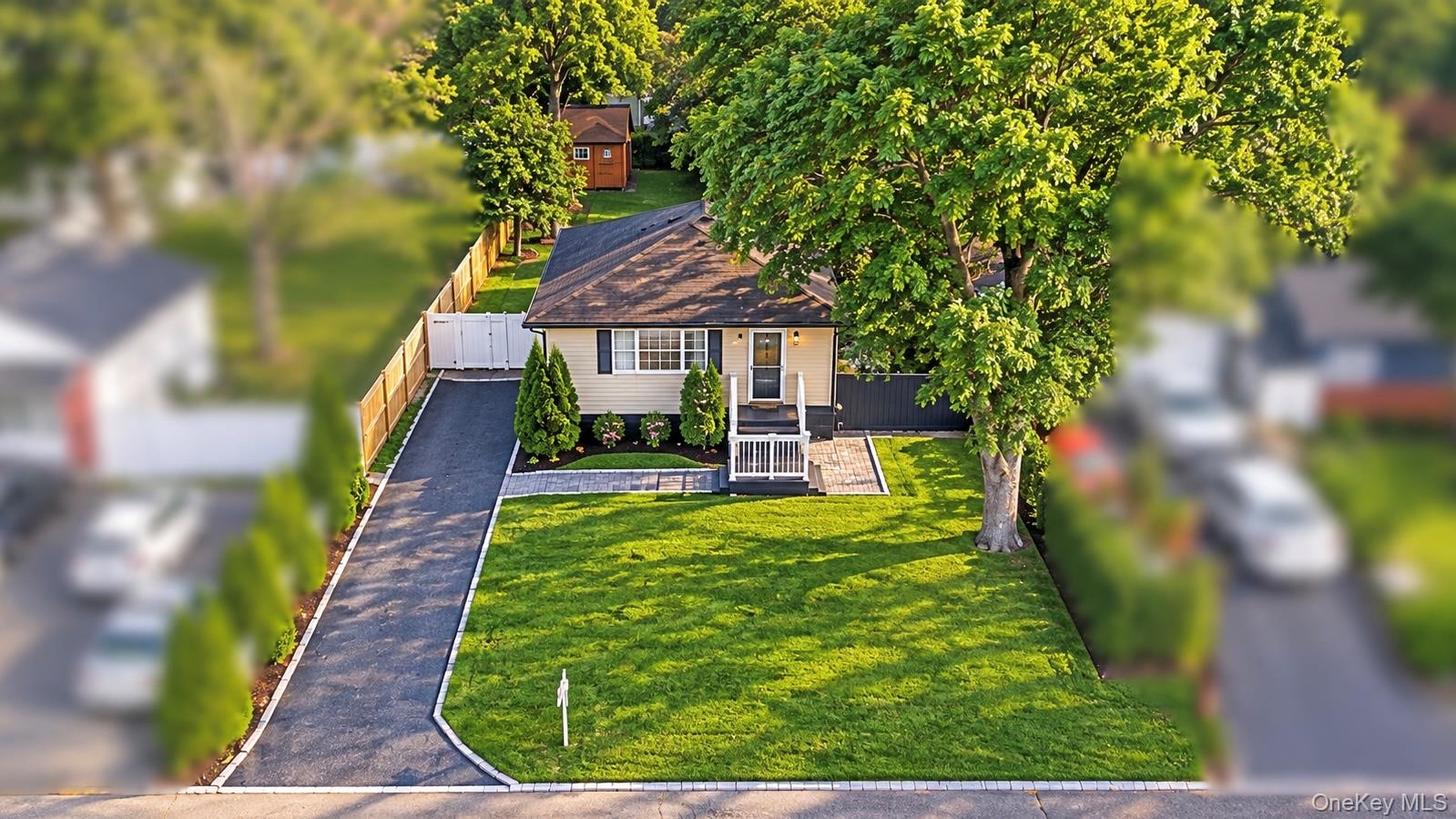 Single-story residence featuring a paved driveway, manicured lawn, stone-paver walkway, wood-fencing, and mature landscaping