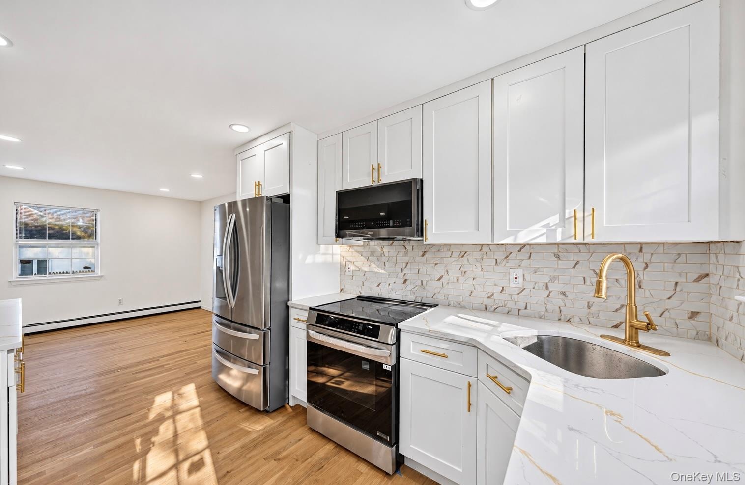 Kitchen featuring white shaker-style cabinetry with gold-tone hardware, stone-surface countertops, decorative tile backsplash, wood-finish flooring, a