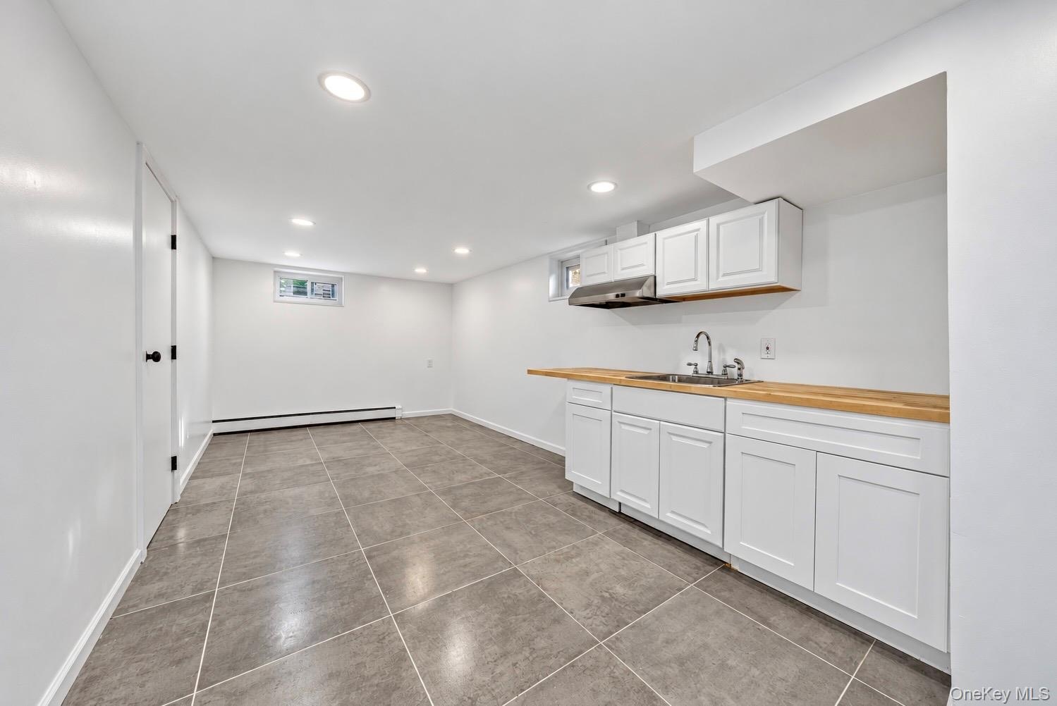 Kitchenette area featuring white shaker-style cabinetry, wood-finish countertops, stainless steel sink, recessed lighting, and tile flooring