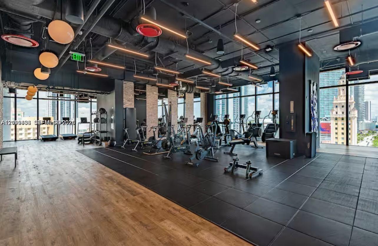 Industrial-style fitness center featuring floor-to-ceiling windows, exposed structural ceiling, wood-finish flooring, rubberized workout surfacing, an