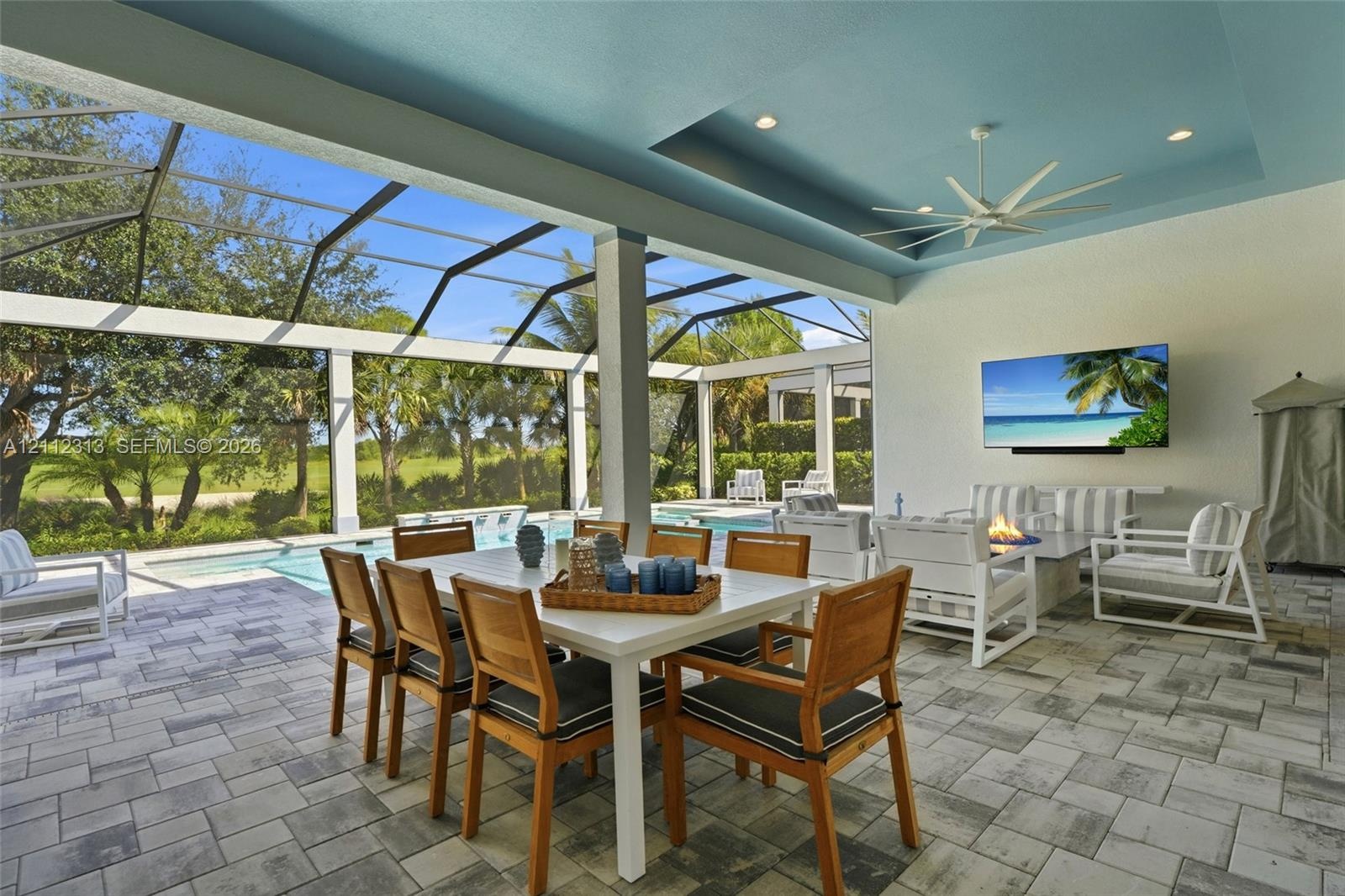 Covered lanai featuring a tray ceiling with recessed lighting, integrated ceiling fan, paver flooring, and a screen enclosure overlooking a swimming p