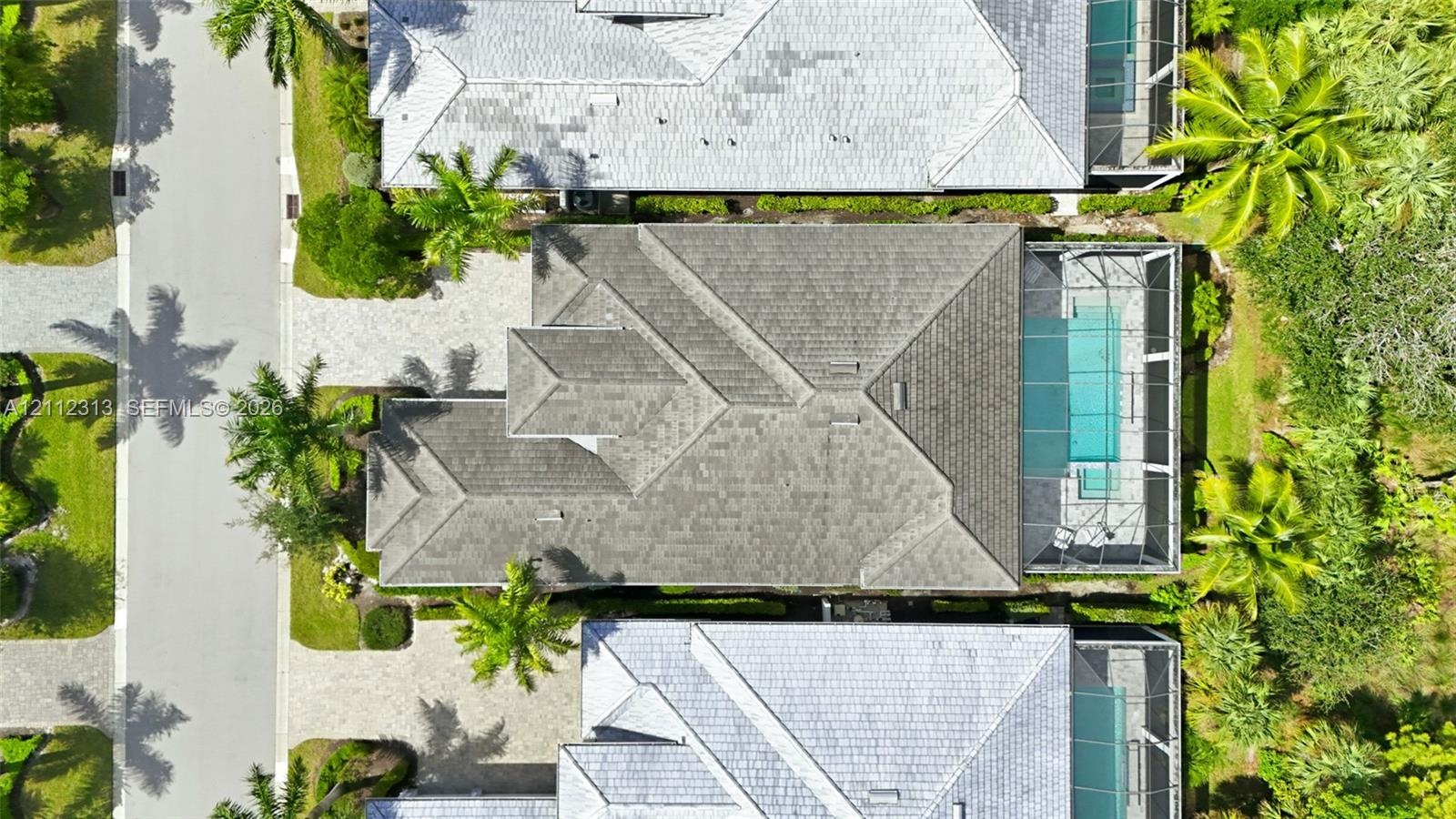 Aerial perspective featuring a multi-hipped roofline, paved driveway, and a screened-in pool enclosure