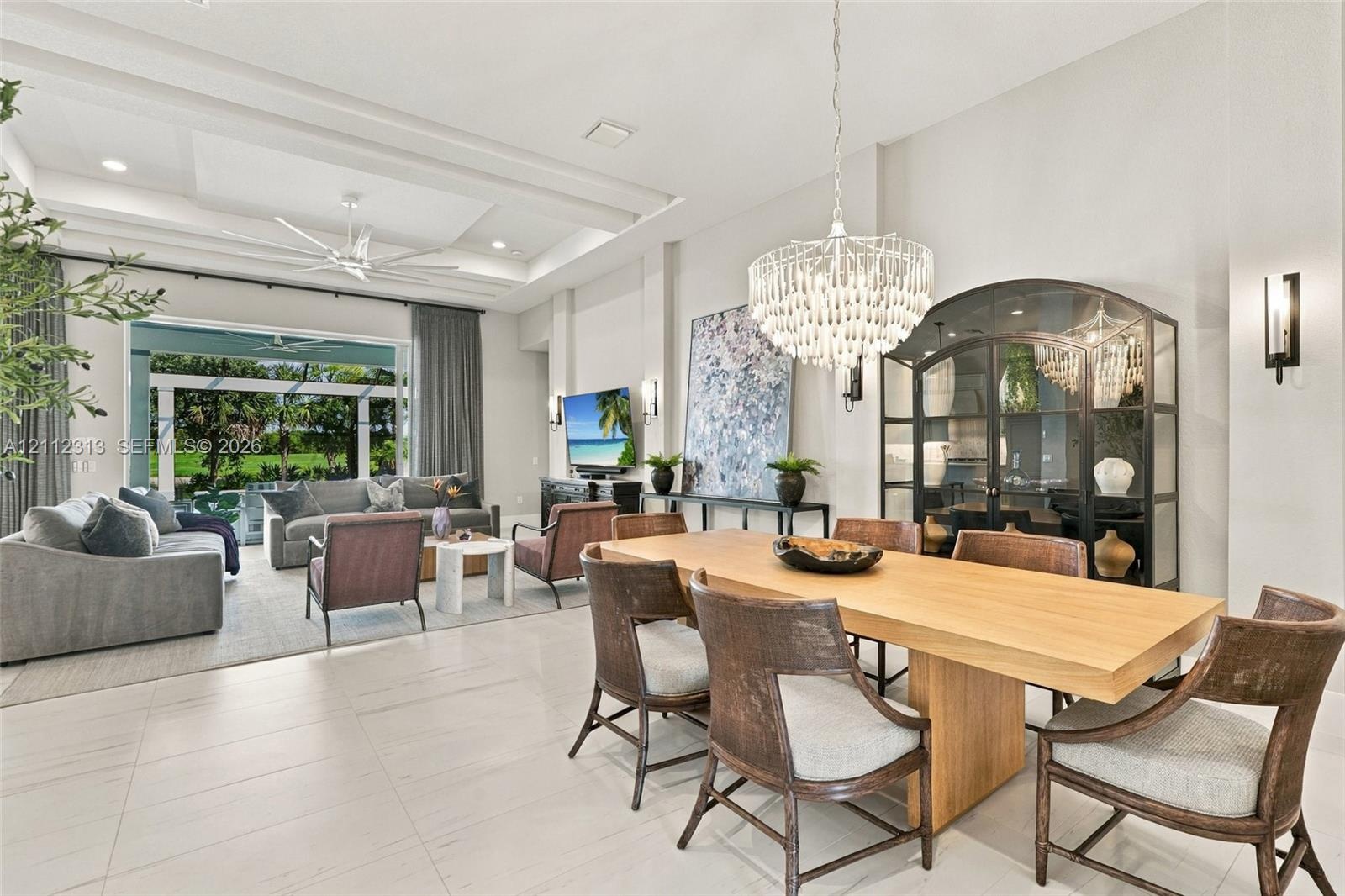 Open-concept living space featuring high tray ceilings, recessed lighting, expansive tile flooring, and a crystal chandelier
