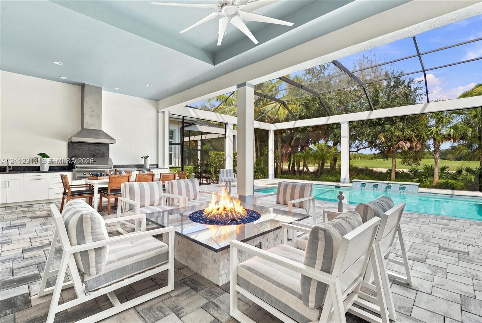 Covered outdoor living area featuring a built-in kitchen with stainless steel range hood, stone-clad fire feature, paver flooring, and a screened-in s