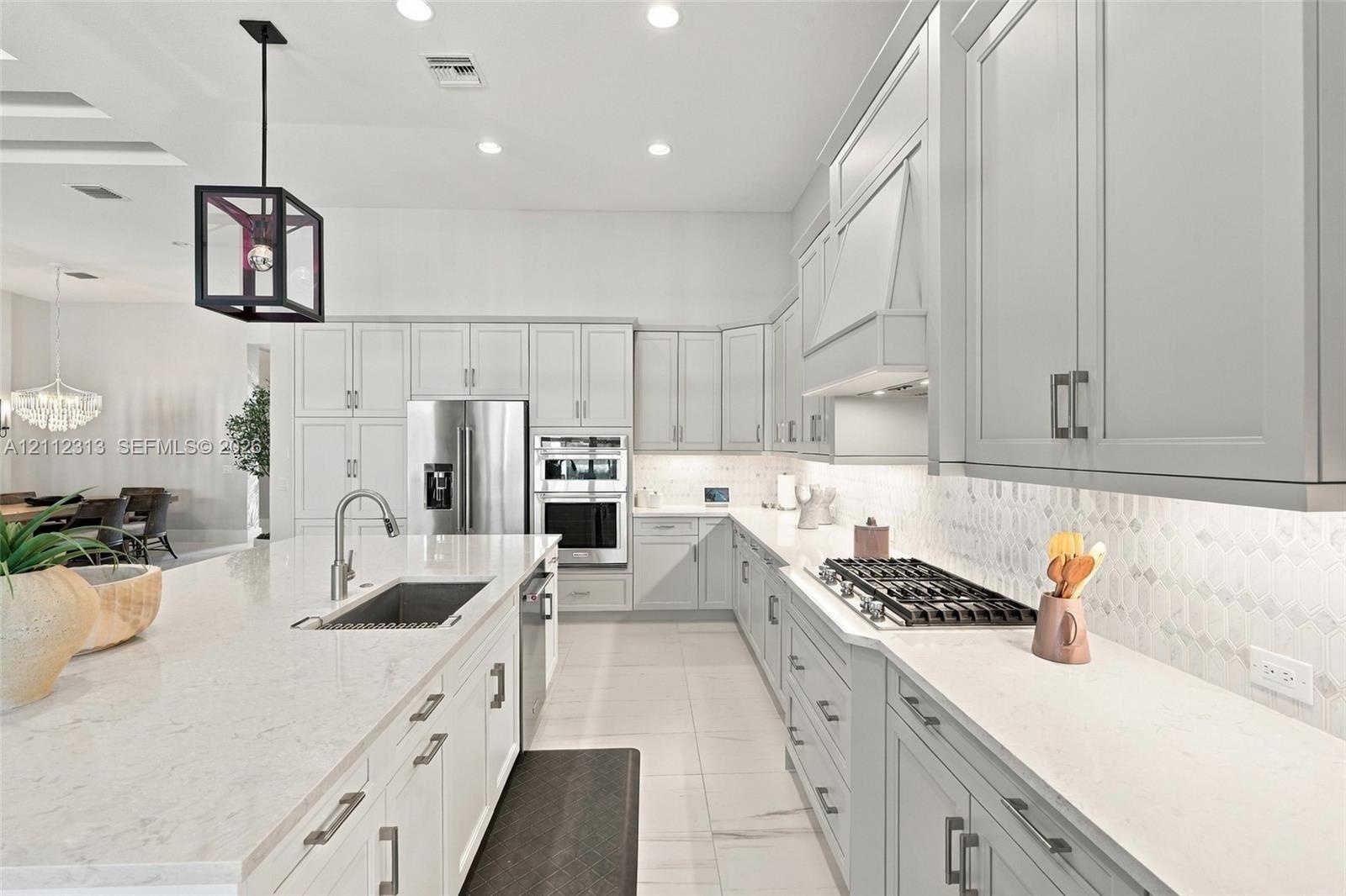 Kitchen featuring light-toned cabinetry, a spacious island with a built-in sink, stone-finish countertops, stainless steel appliances, and a geometric