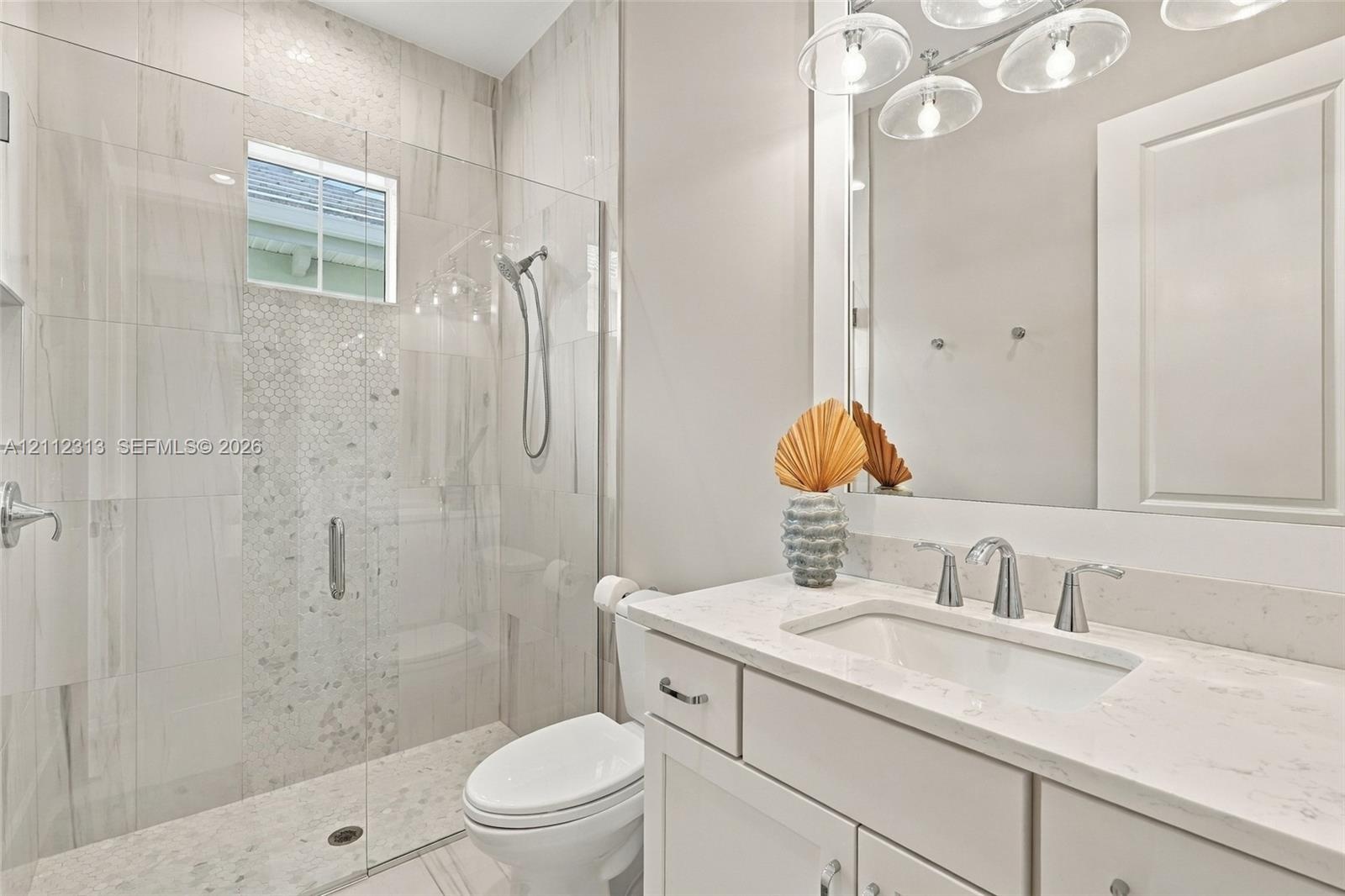 Bathroom featuring a vanity with a white countertop and undermount sink, a walk-in shower with a glass enclosure, floor-to-ceiling tilework, and a mul