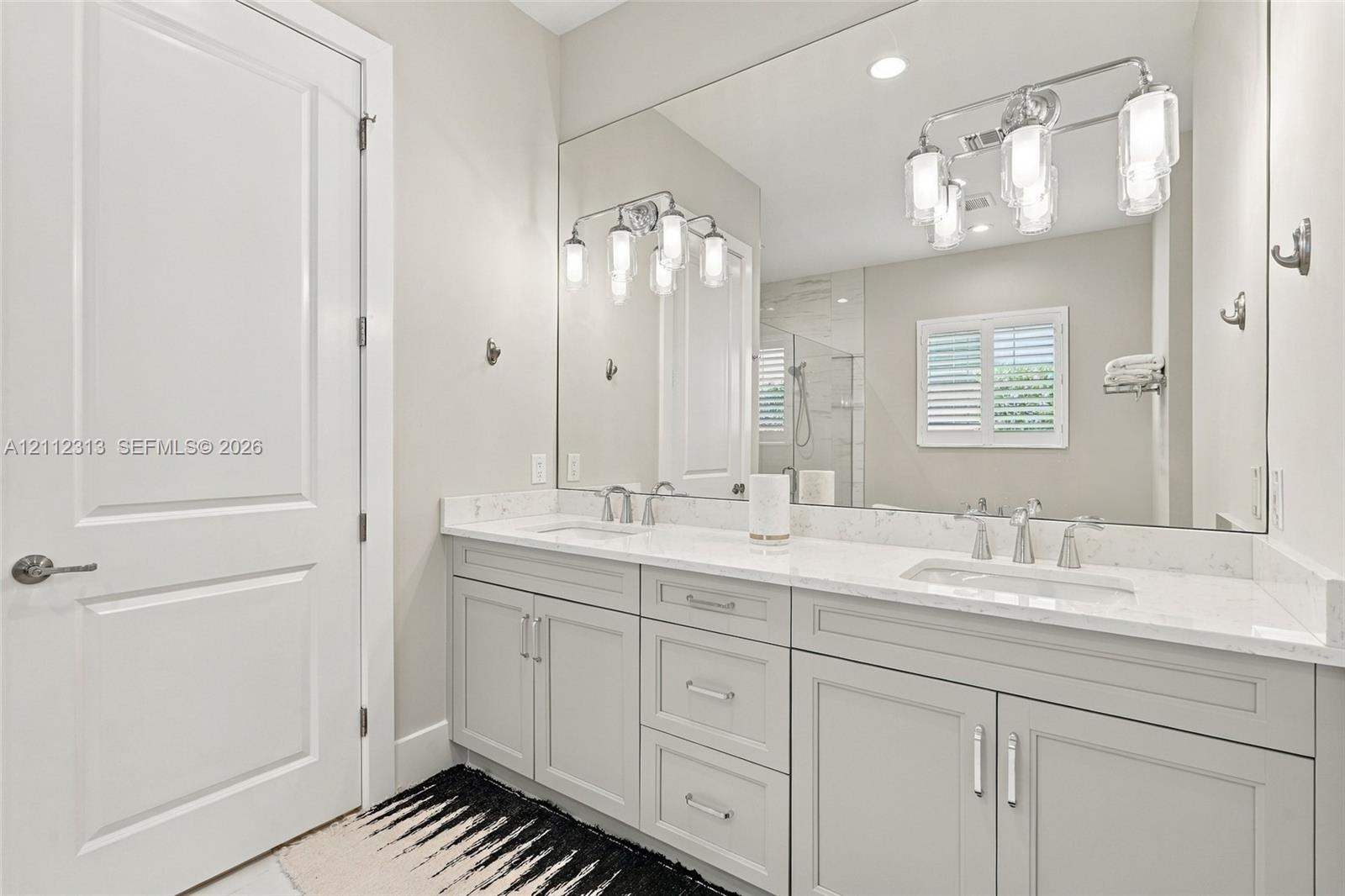 Double vanity featuring light-toned cabinetry, stone-finish countertops, undermount sinks, polished metal fixtures, and a wall-to-wall mirror with mul