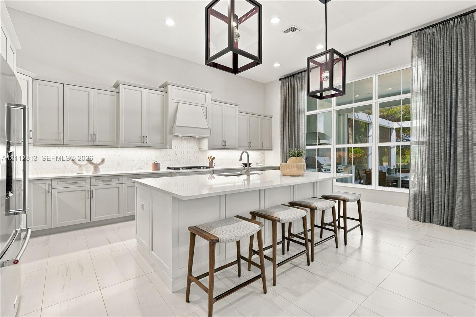 Kitchen featuring light-toned cabinetry, a large central island with a solid surface countertop, tile flooring, recessed lighting, and geometric penda