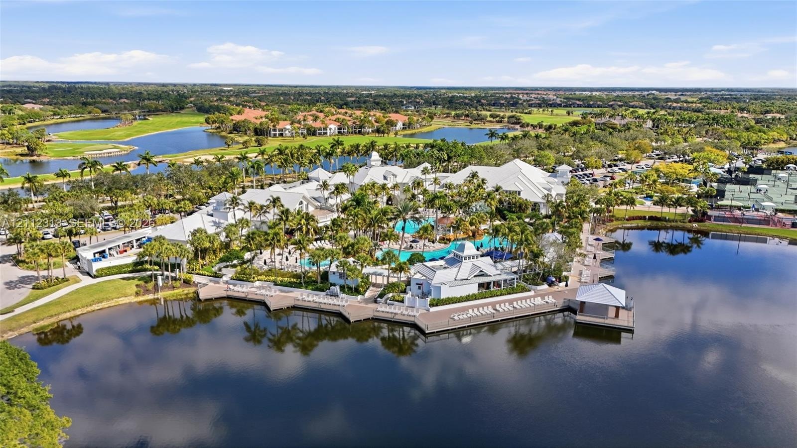 Aerial view of a coastal-inspired complex featuring a resort-style swimming pool, expansive waterfront sun deck, multi-tiered white roofing, and manic