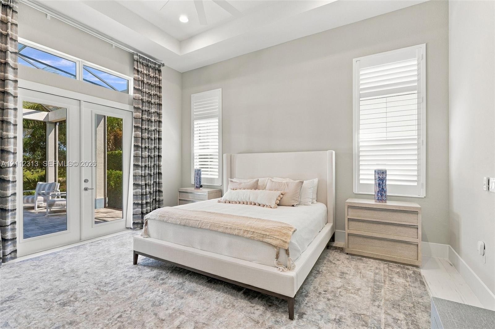 Tray ceiling with recessed lighting, floor-to-ceiling glass French doors, transom windows, and white plantation shutters