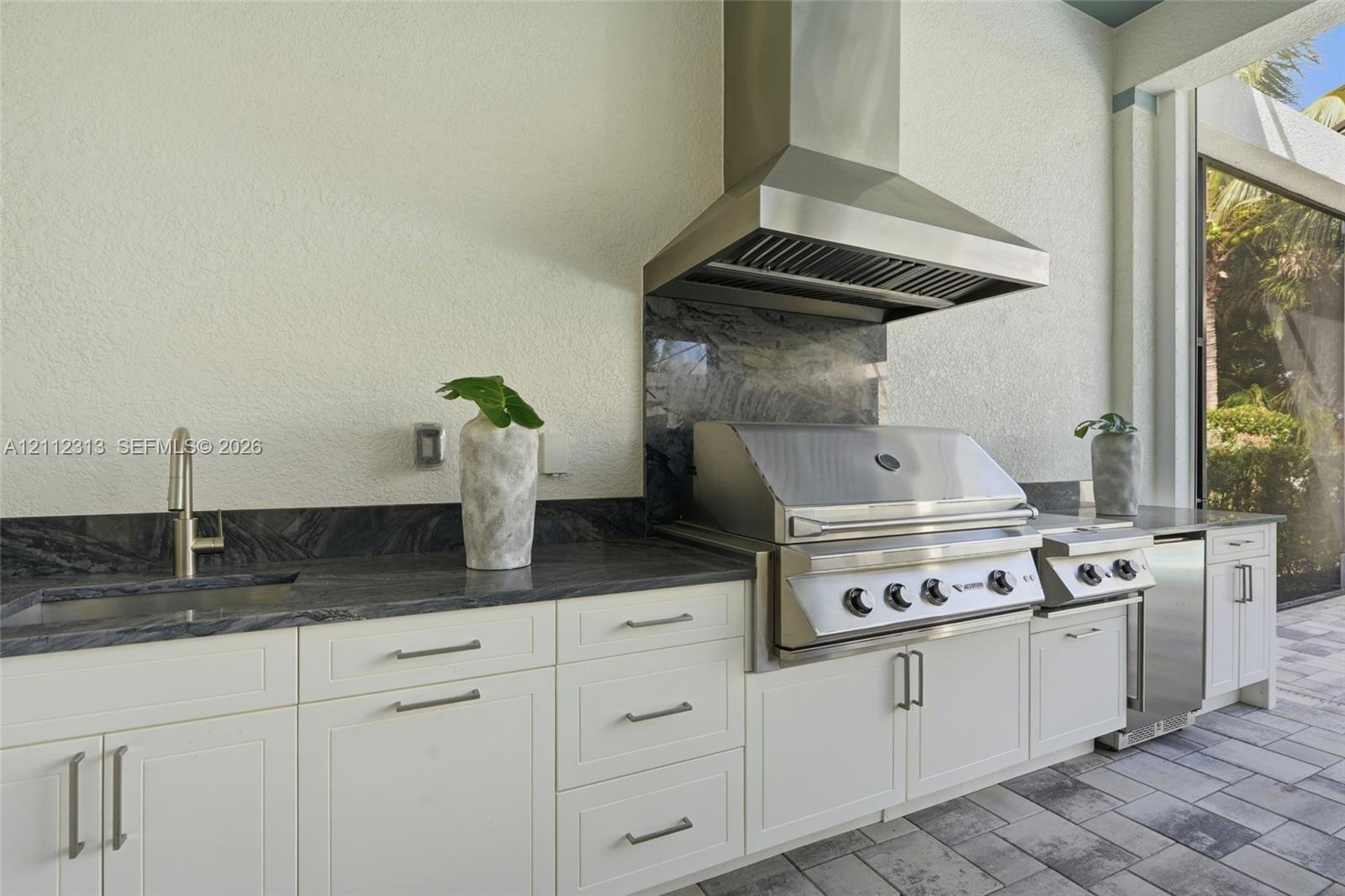 Outdoor kitchen featuring white shaker-style cabinetry, dark natural stone countertops and backsplash, stainless steel built-in grill, commercial-grad