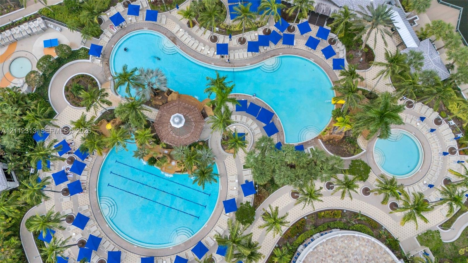 Aerial view of a sprawling pool complex featuring multiple swimming pools, a dedicated lap lane section, a central gazebo, and expansive paved decking