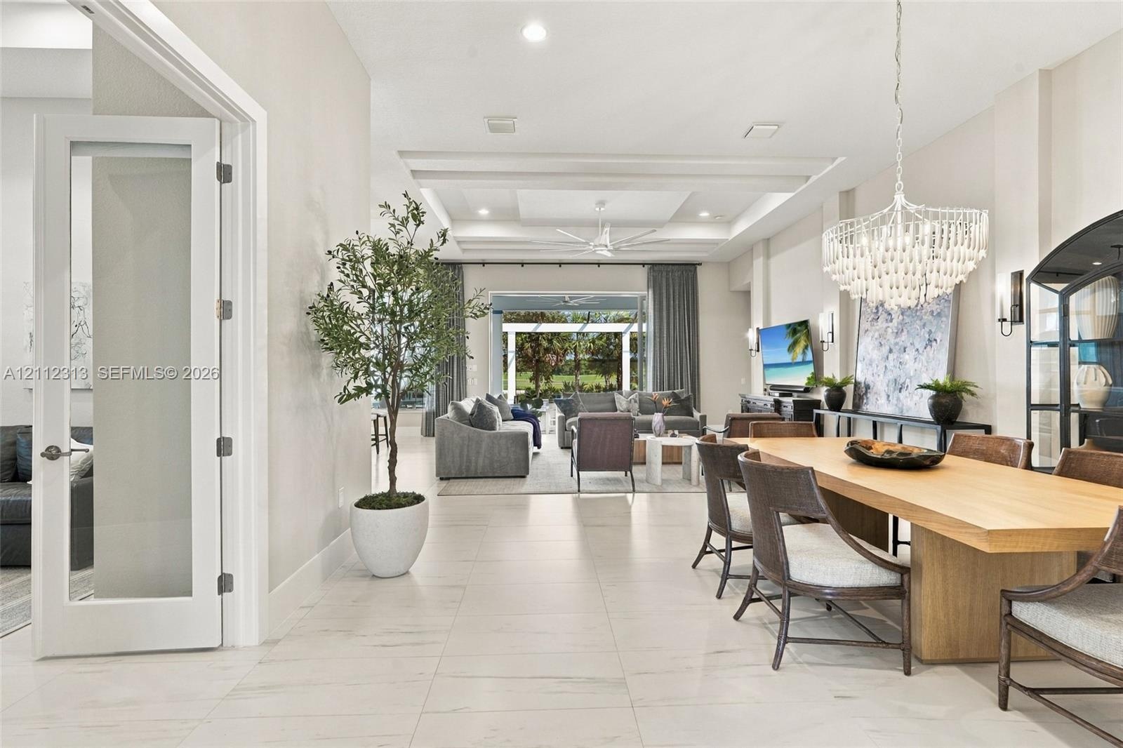 Open-concept interior featuring large-format tile flooring, tray ceilings with recessed lighting, and a crystal chandelier