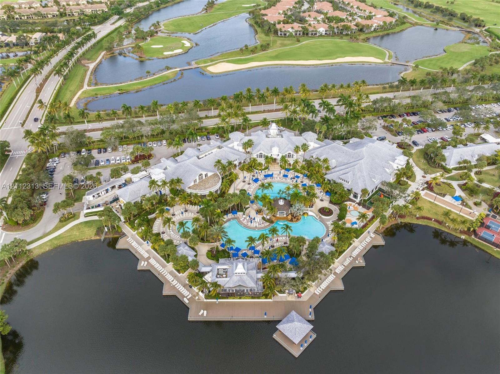 Aerial perspective of a multi-structure facility featuring a complex of resort-style swimming pools, expansive paved sun decks, a waterfront gazebo, a
