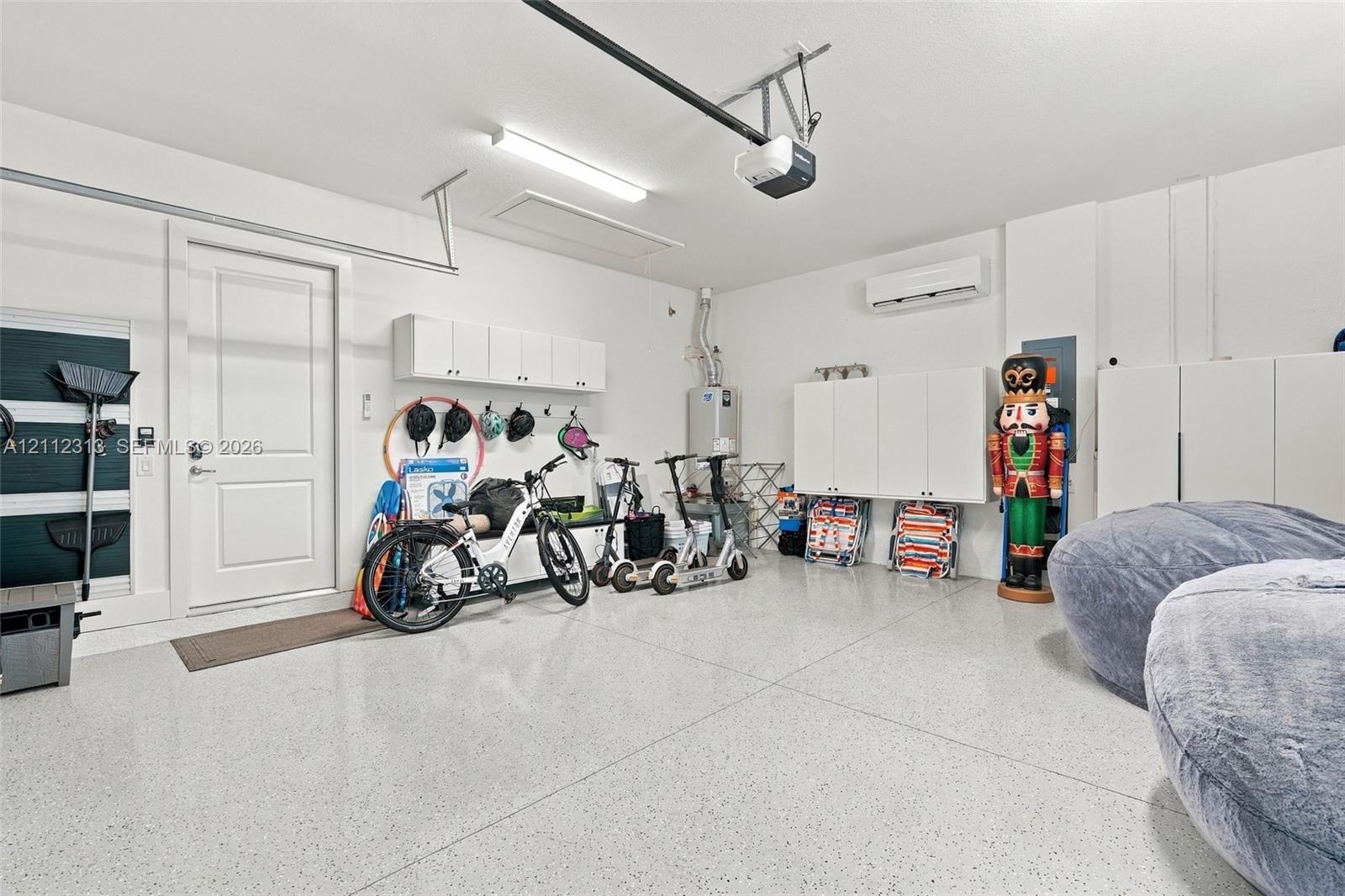Garage featuring epoxy-coated flooring, wall-mounted white storage cabinetry, an installed climate control unit, and an automated garage door opener s