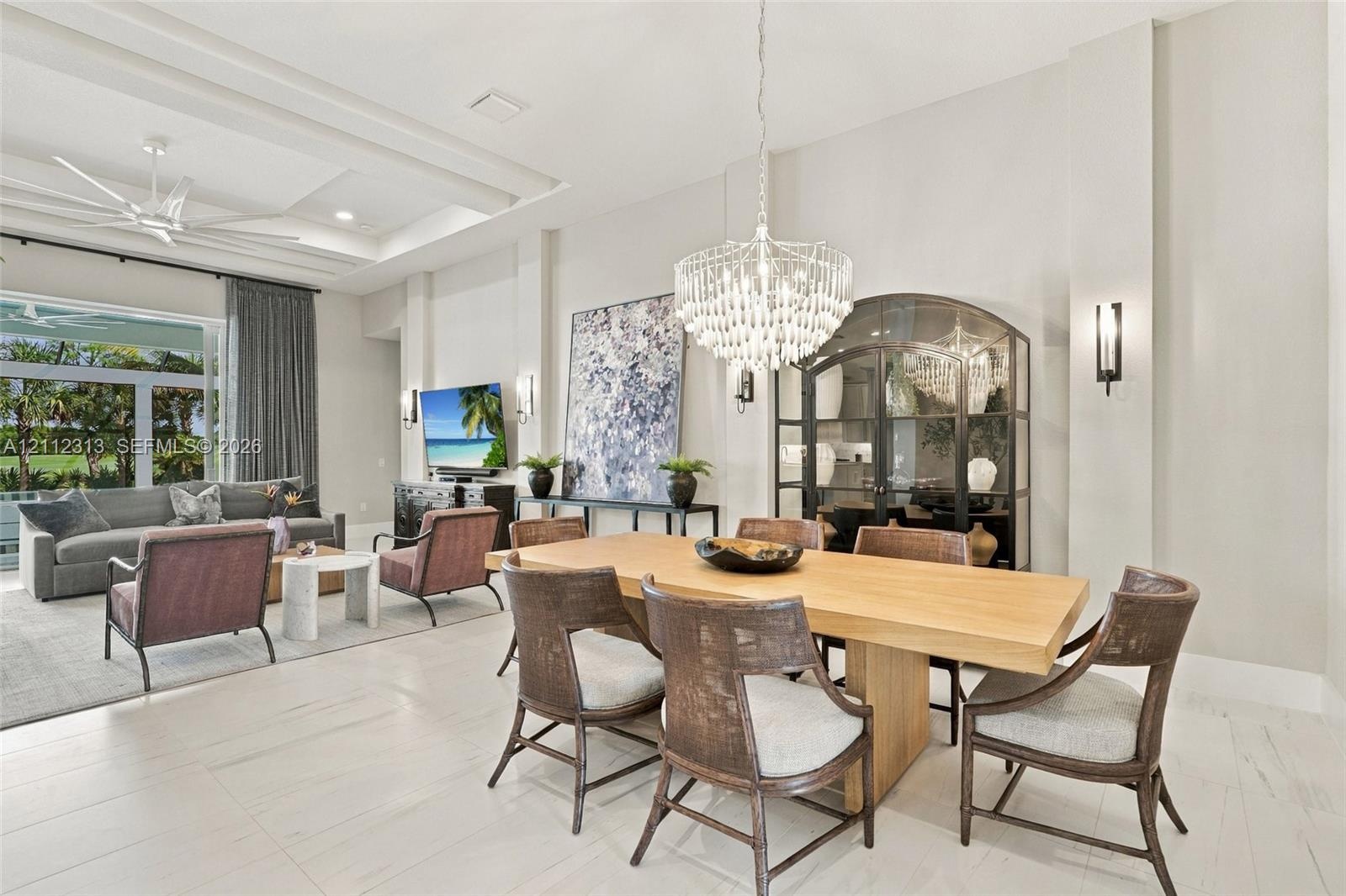 Tray ceilings, light-tone flooring, built-in arched glass display cabinetry, tiered crystal chandelier, and wall-mounted sconce lighting