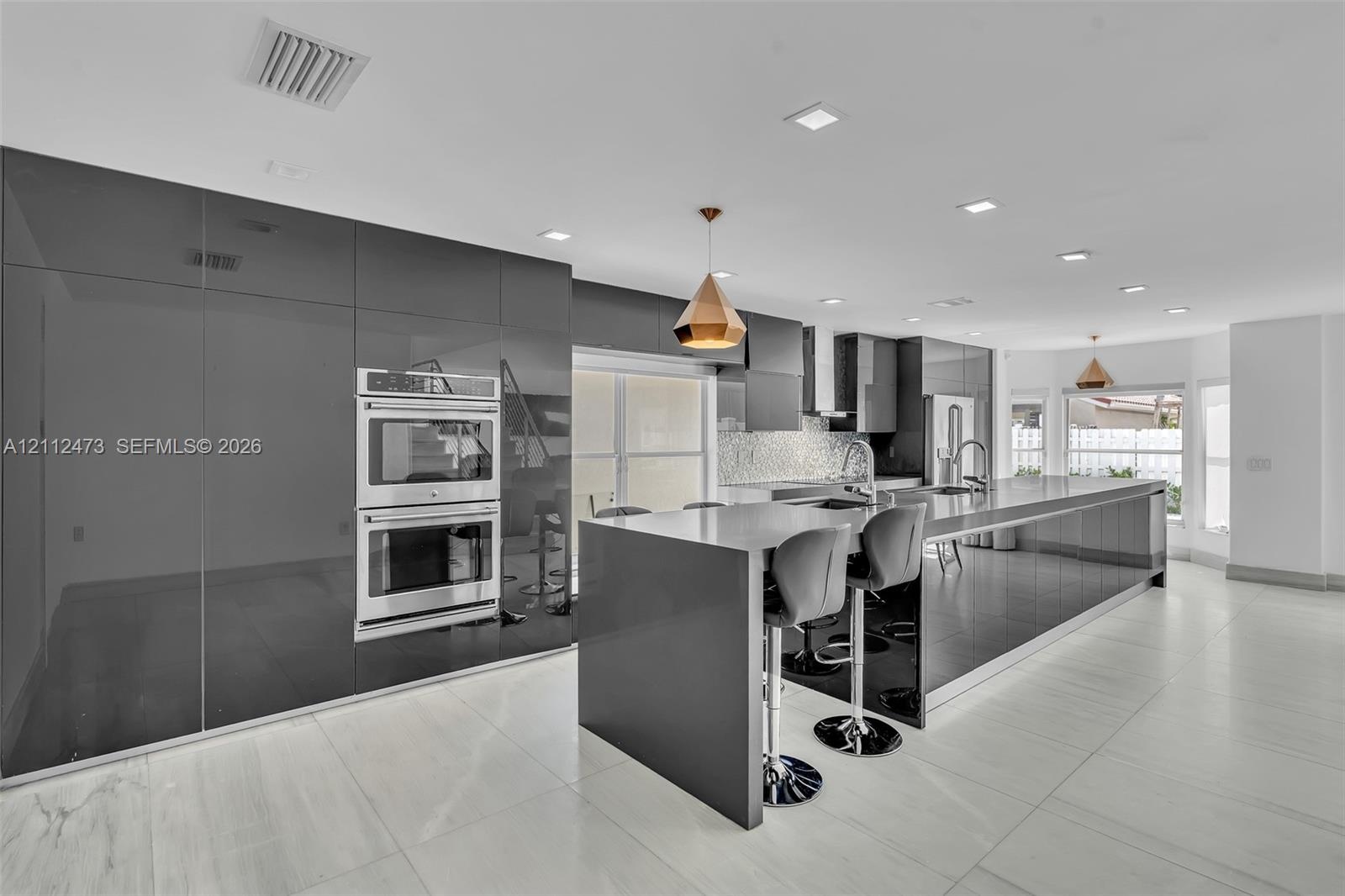 Contemporary kitchen featuring high-gloss cabinetry, stainless steel double wall ovens, a large kitchen island with quartz countertops, recessed light
