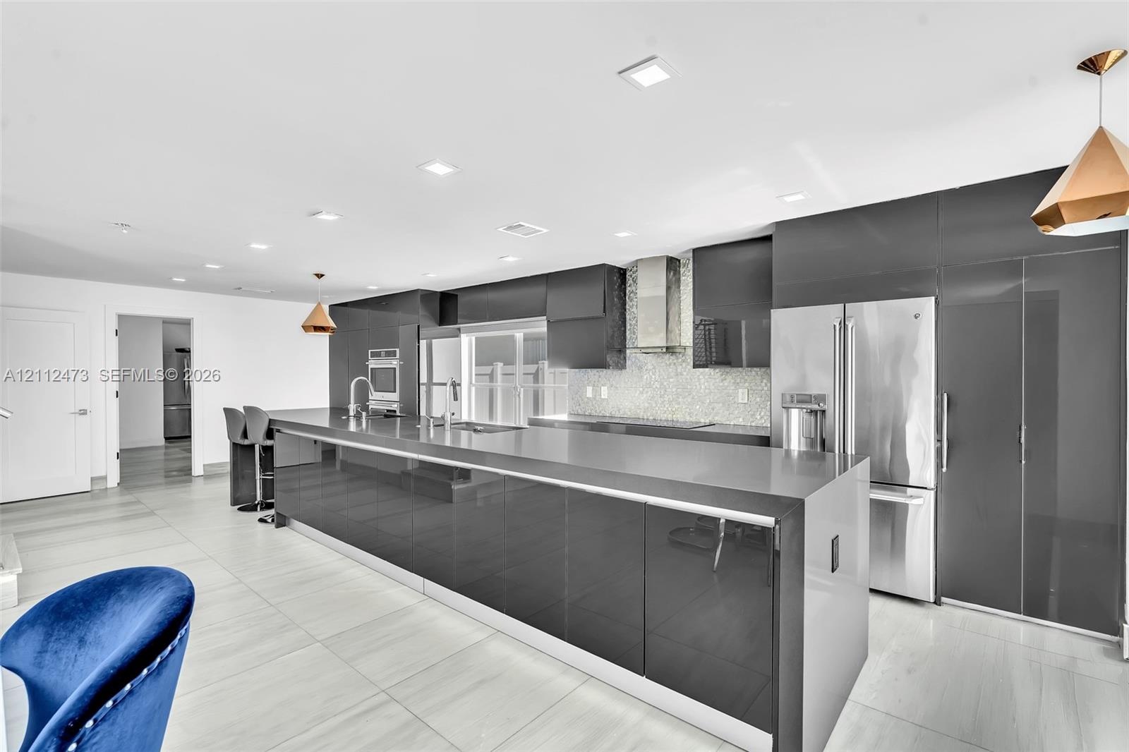 Contemporary kitchen featuring high-gloss cabinetry, stainless steel appliances, a stone countertop island, recessed lighting, and large-format tile f