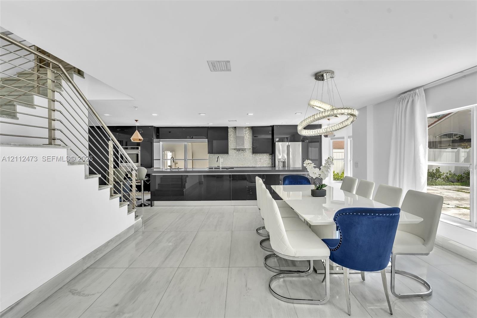 Open-concept interior featuring large-format tile flooring, high-gloss cabinetry, stainless steel range hood, stainless steel horizontal railing stair
