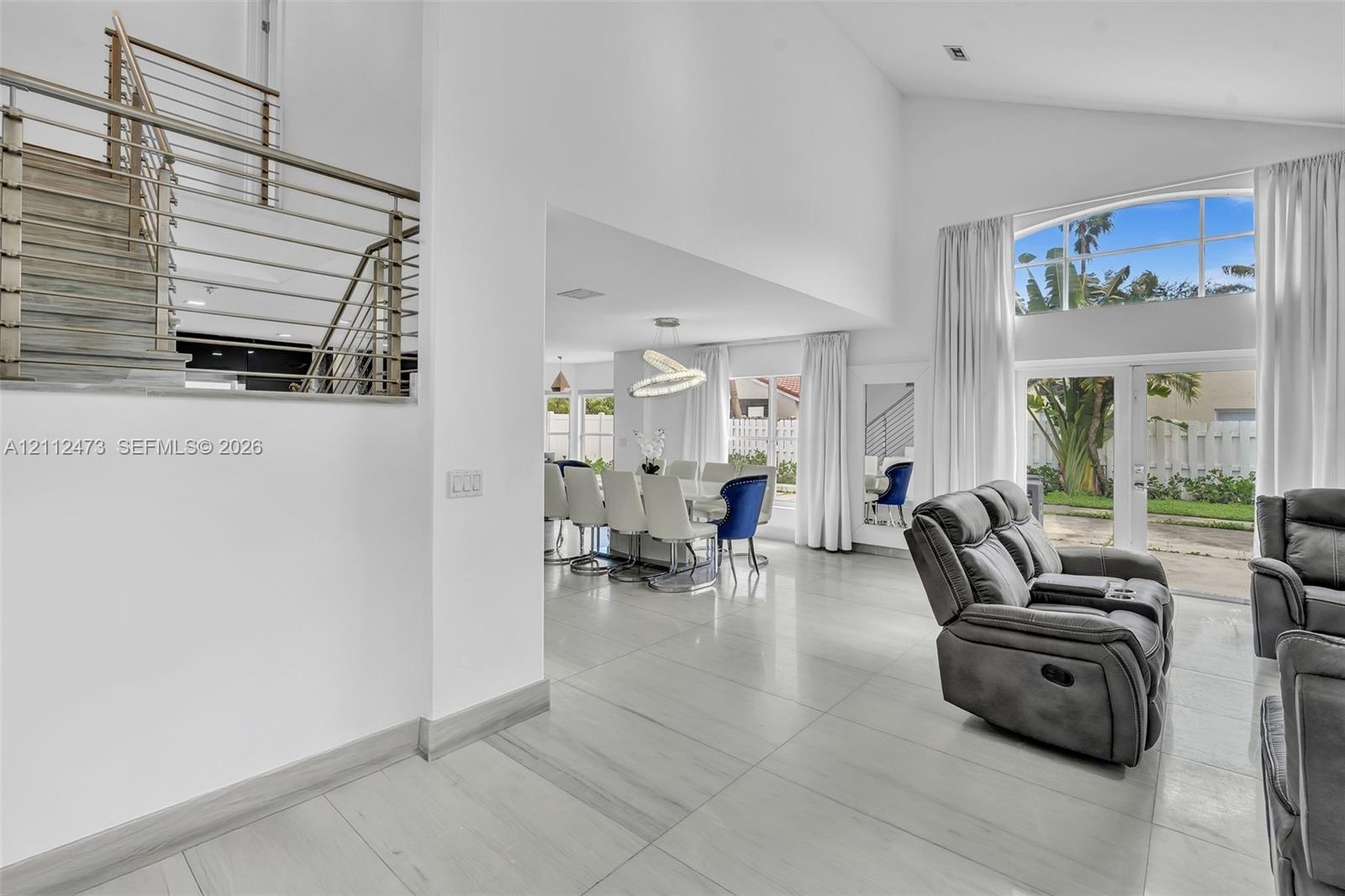 Vaulted ceilings, large-format tile flooring, a metal stair railing, and expansive glass window panels with exterior access