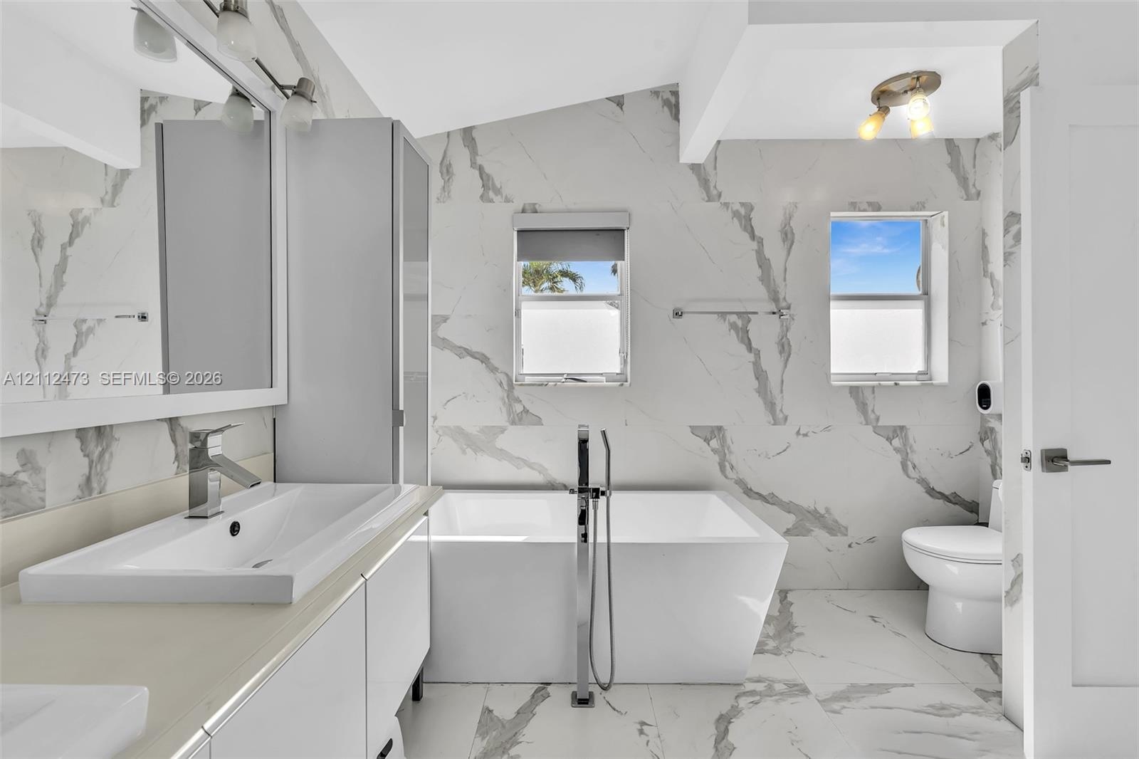 Bathroom featuring floor-to-ceiling large-format tile with decorative veining, freestanding soaking tub with floor-mounted faucet, rectangular vessel 