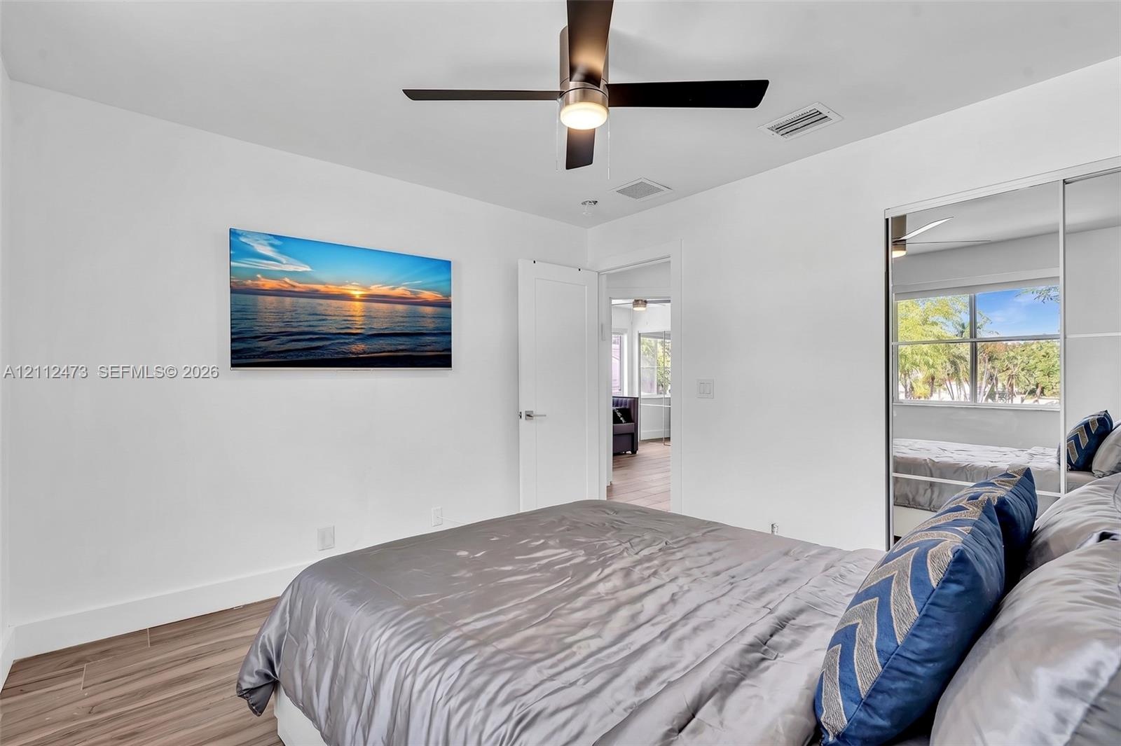 Wood-finish flooring, ceiling fan with integrated lighting, and sliding mirror-paneled closet doors