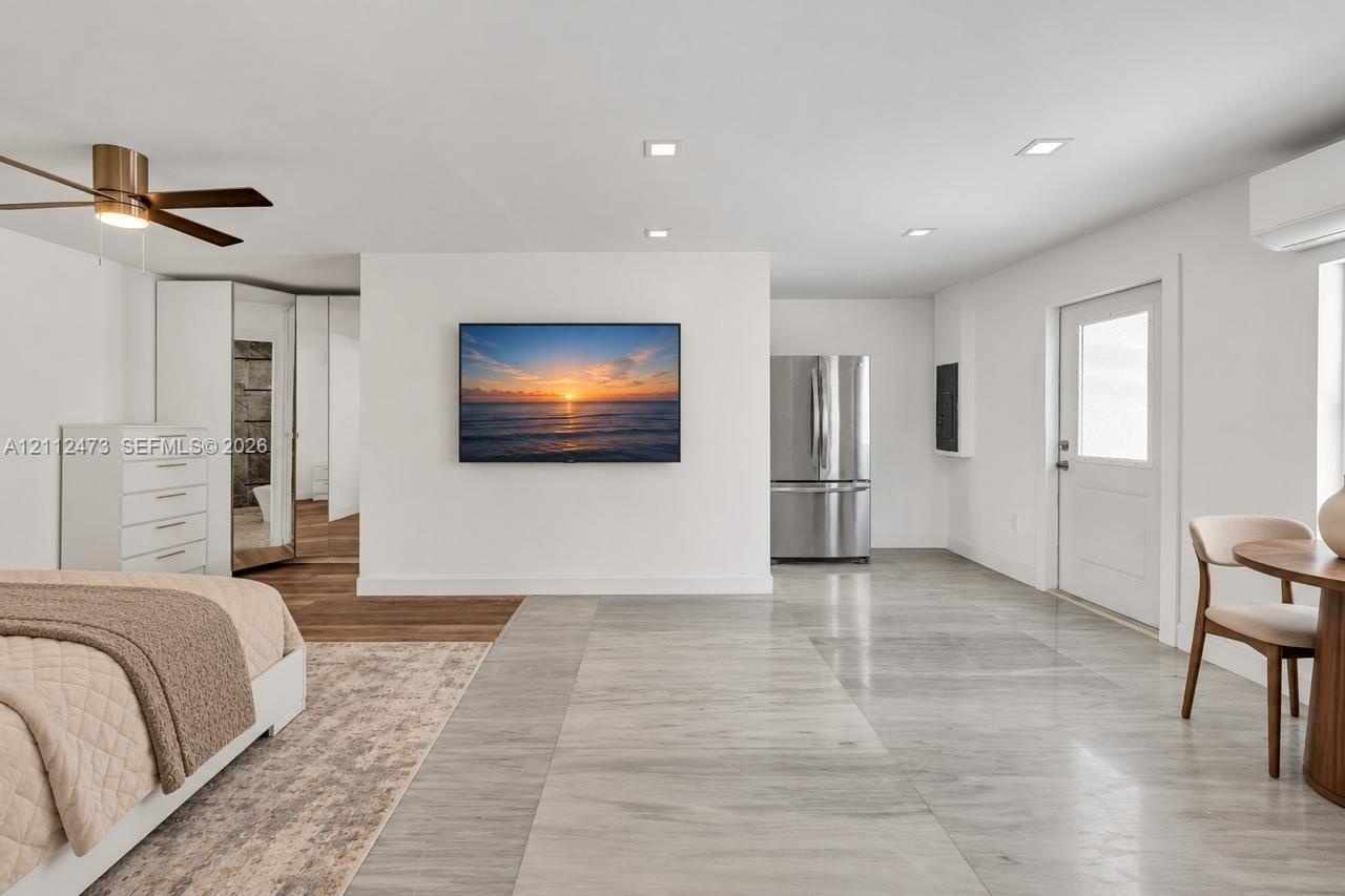 Light-toned tile flooring, recessed ceiling lighting, brushed metallic ceiling fan, stainless steel refrigerator, and wall-mounted climate control uni
