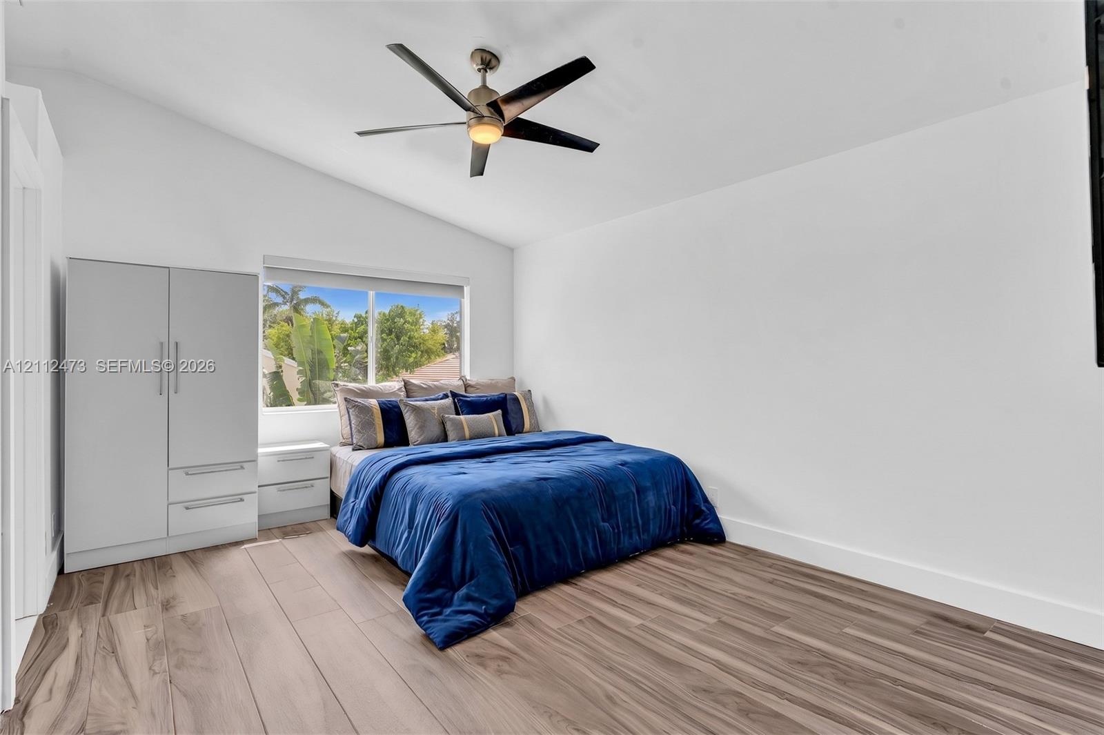 Vaulted ceiling featuring a central five-blade ceiling fan, wood-finish flooring, and a large picture window
