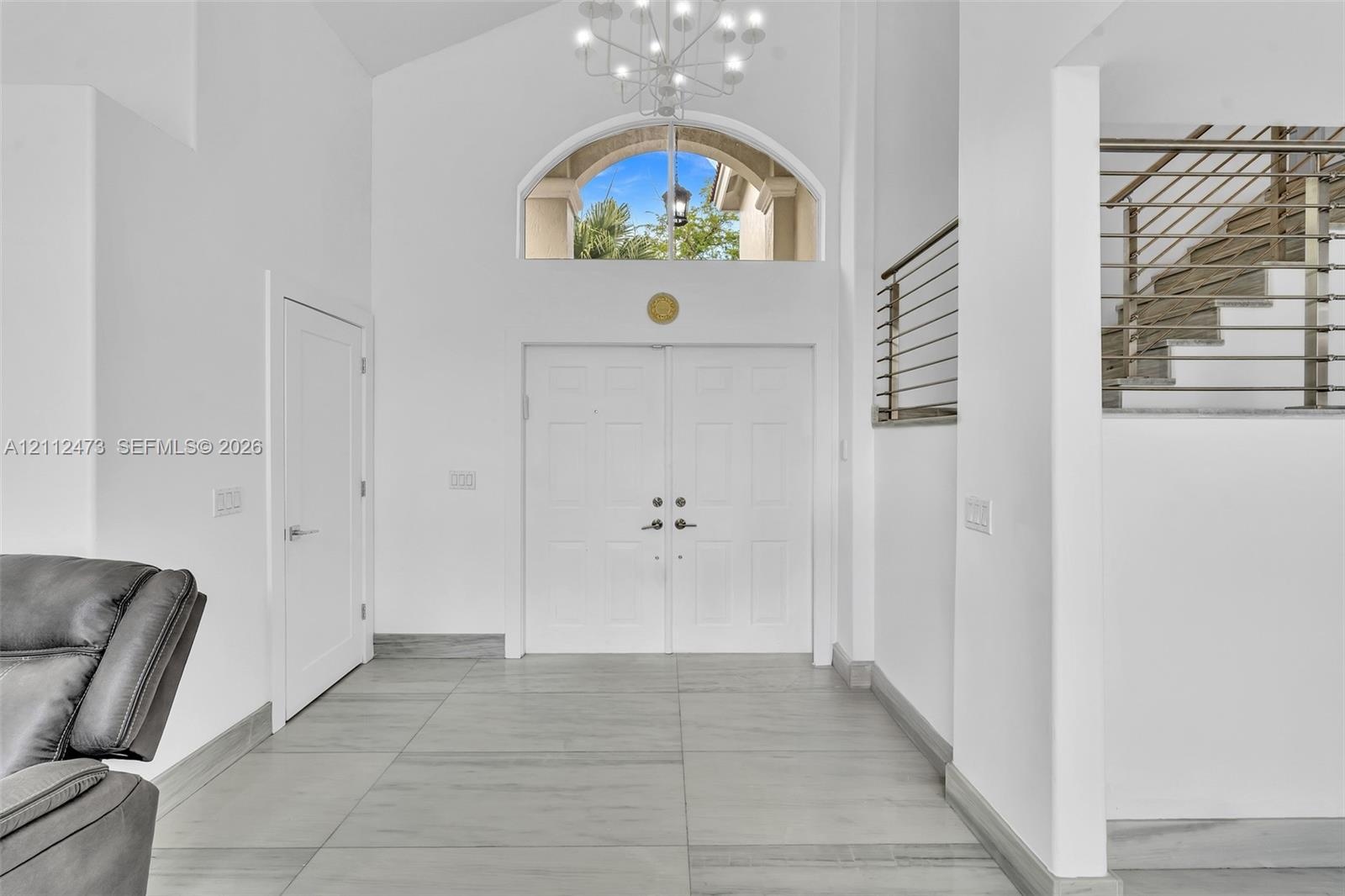 Double-door entryway featuring vaulted ceilings, a prominent arched transom window, a contemporary multi-arm chandelier, and metal horizontal-bar rail
