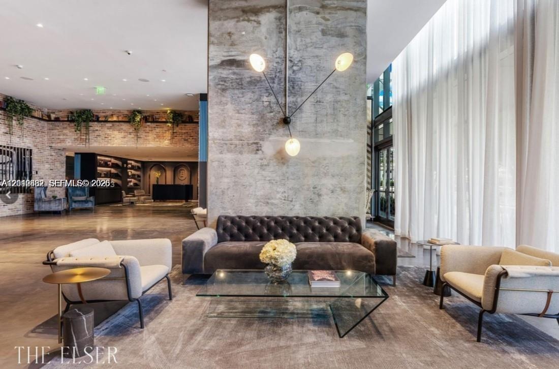 Exposed concrete accent wall with multi-arm fixture, floor-to-ceiling drapery, polished concrete flooring, and decorative brick masonry wall