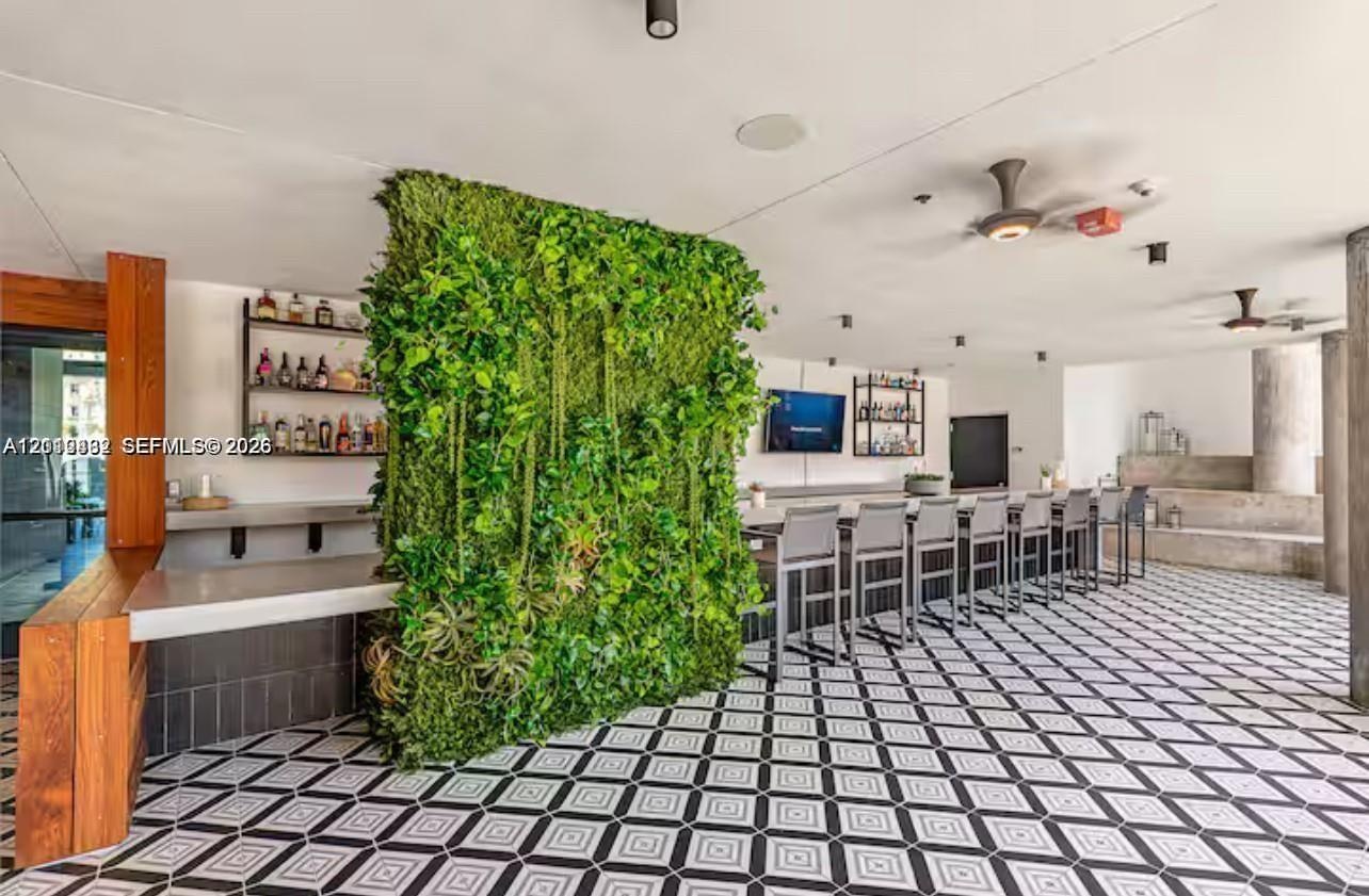 Covered outdoor bar area featuring a geometric-pattern tile floor, a vertical greenery wall, built-in counter seating, and wood-accented structural pi