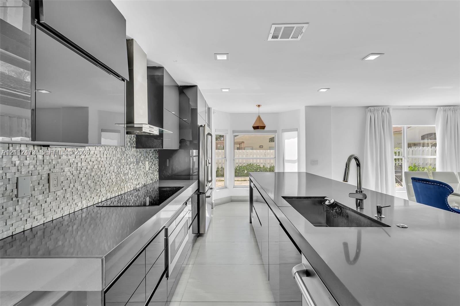 Modern kitchen featuring high-gloss cabinetry, stone countertops, a mosaic tile backsplash, a stainless steel range hood, and a large central island w