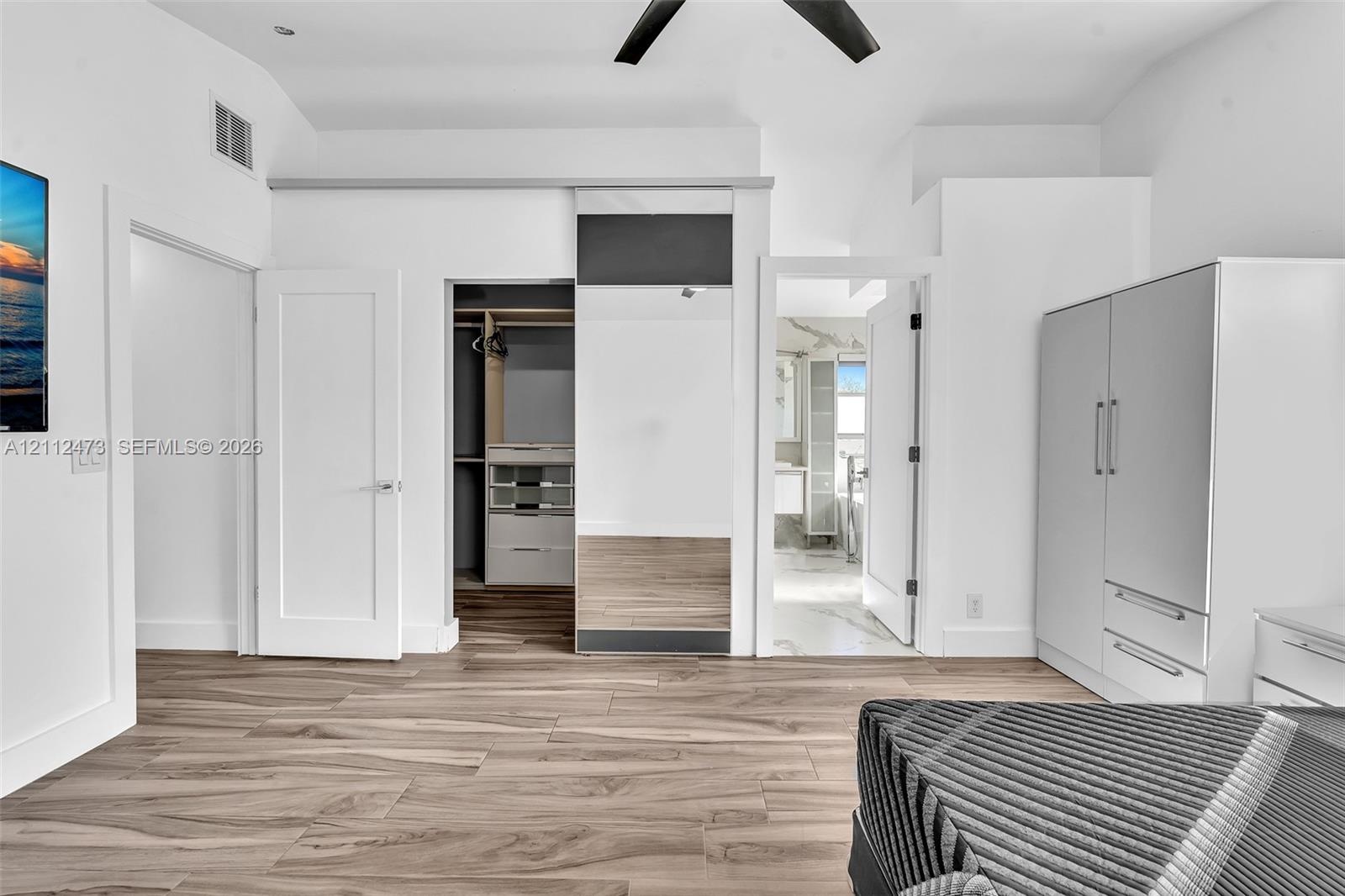 Wood-finish flooring, vaulted ceiling with a matte black fan, sliding mirrored closet door, and built-in closet organization system
