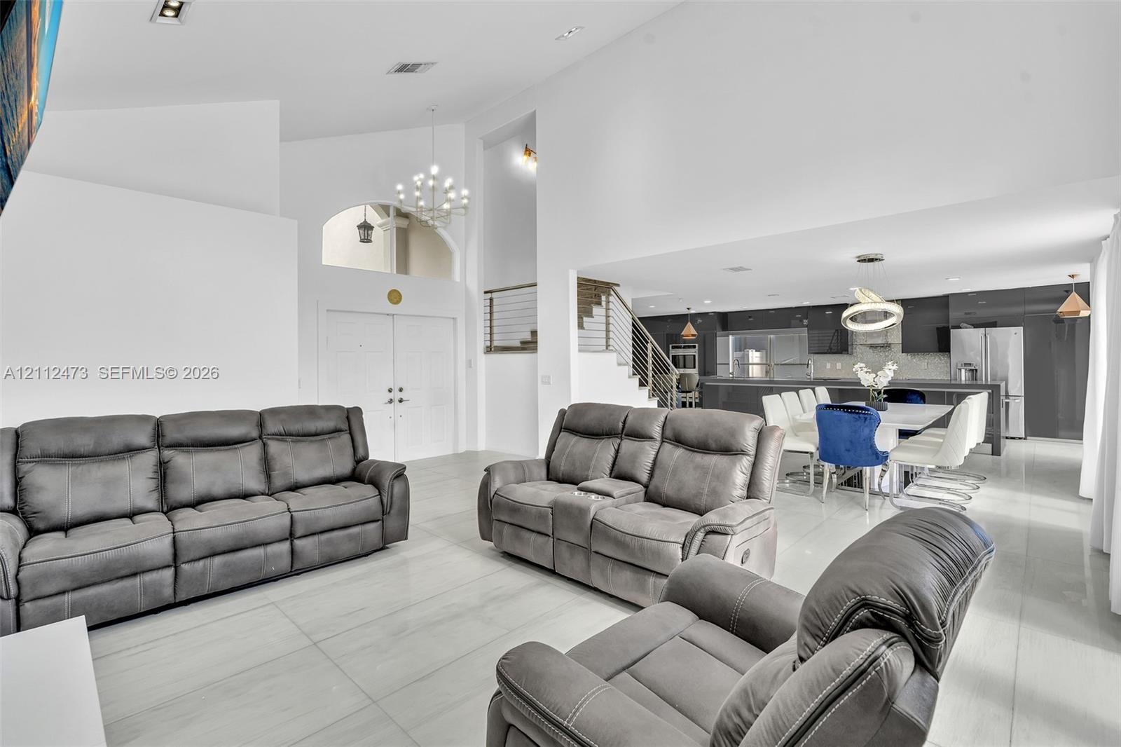 Vaulted ceilings, large-format tile flooring, a built-in staircase with a metal railing, recessed lighting, and a modern kitchen featuring a central i