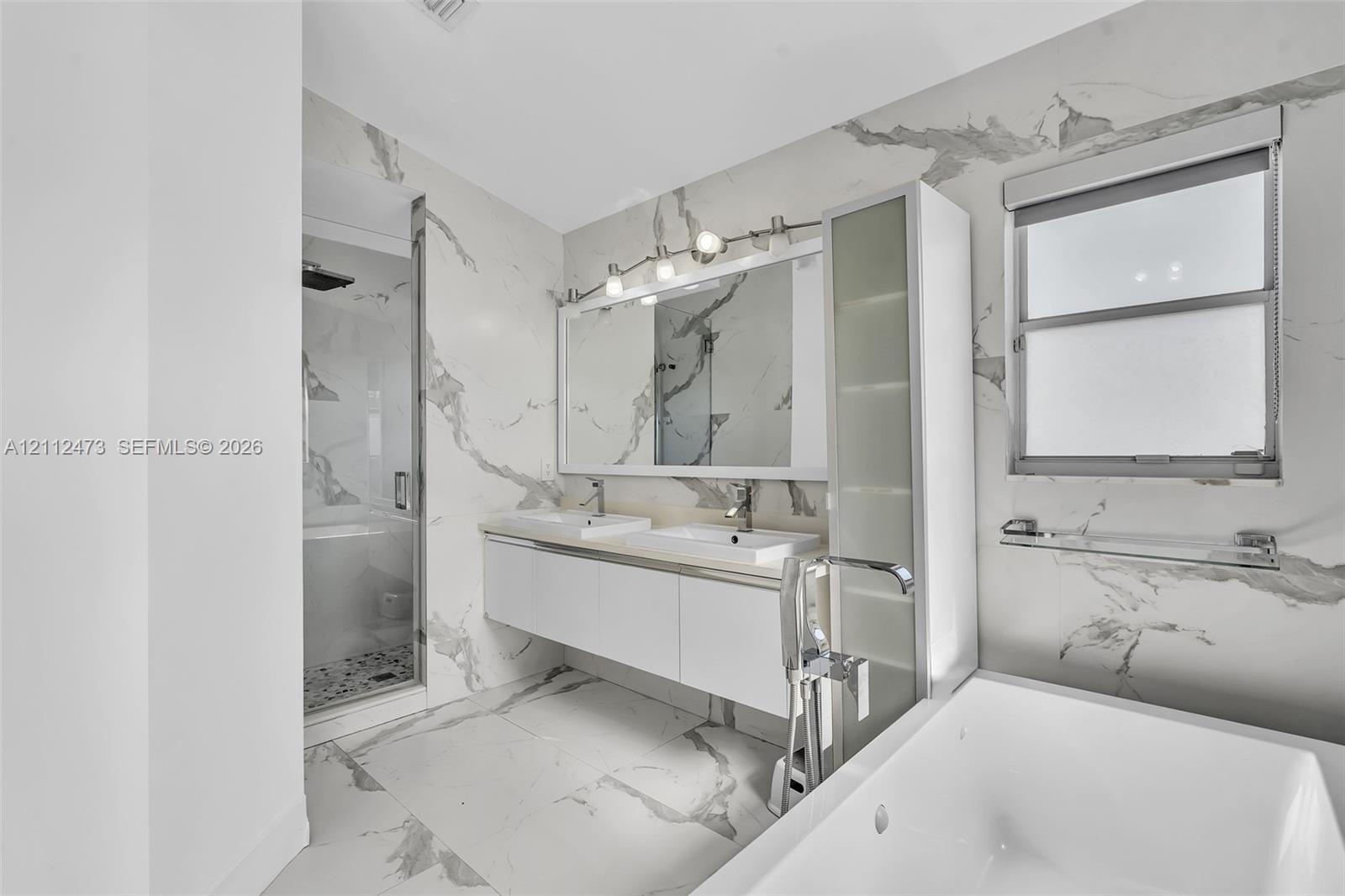 Bathroom featuring floor-to-ceiling large-format stone-patterned wall tile, white floating double vanity with integrated sinks, glass-enclosed walk-in