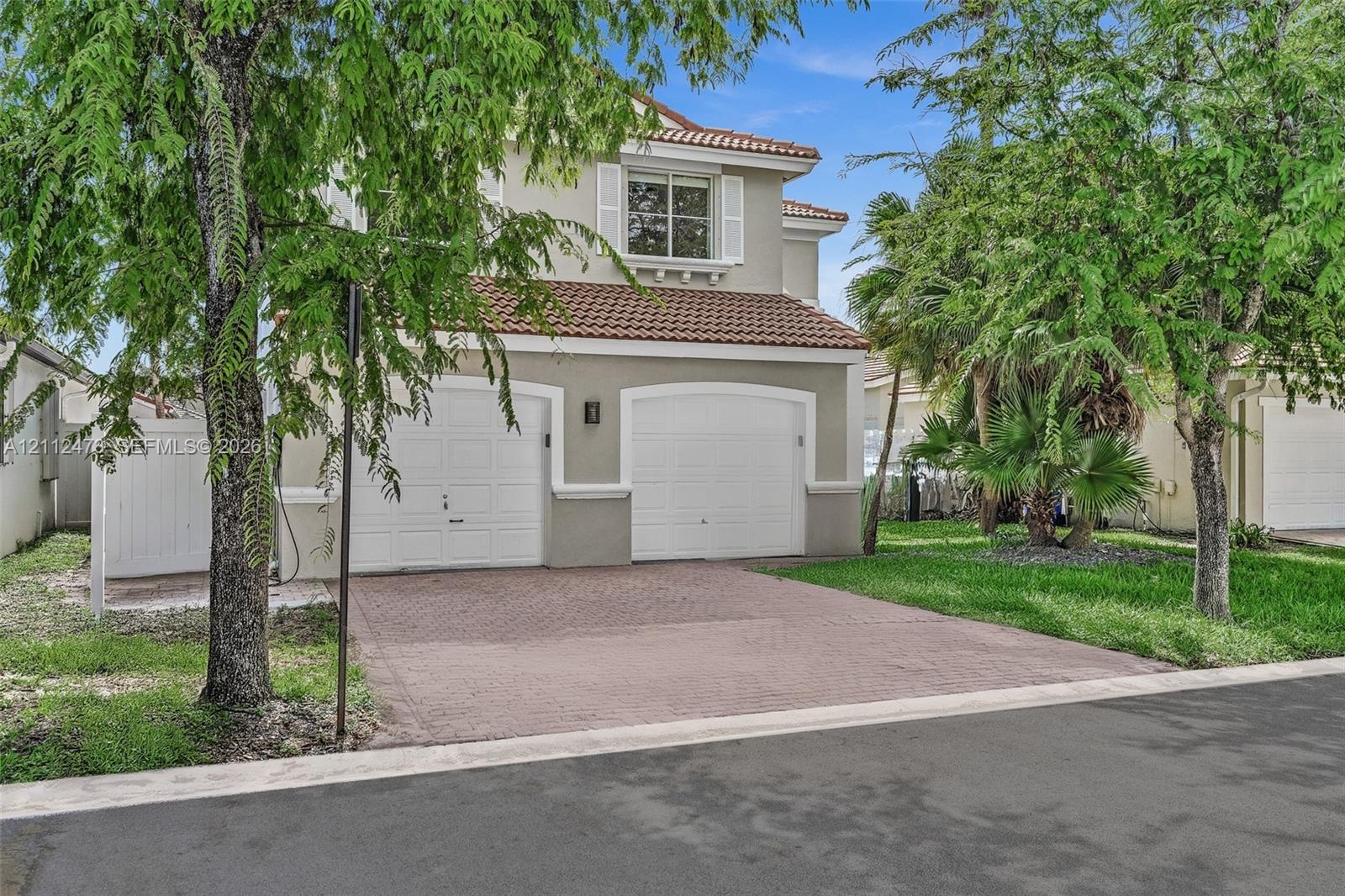 Two-story exterior featuring a clay tile roof, stucco siding, arched garage doors, a paved driveway, and decorative window shutters